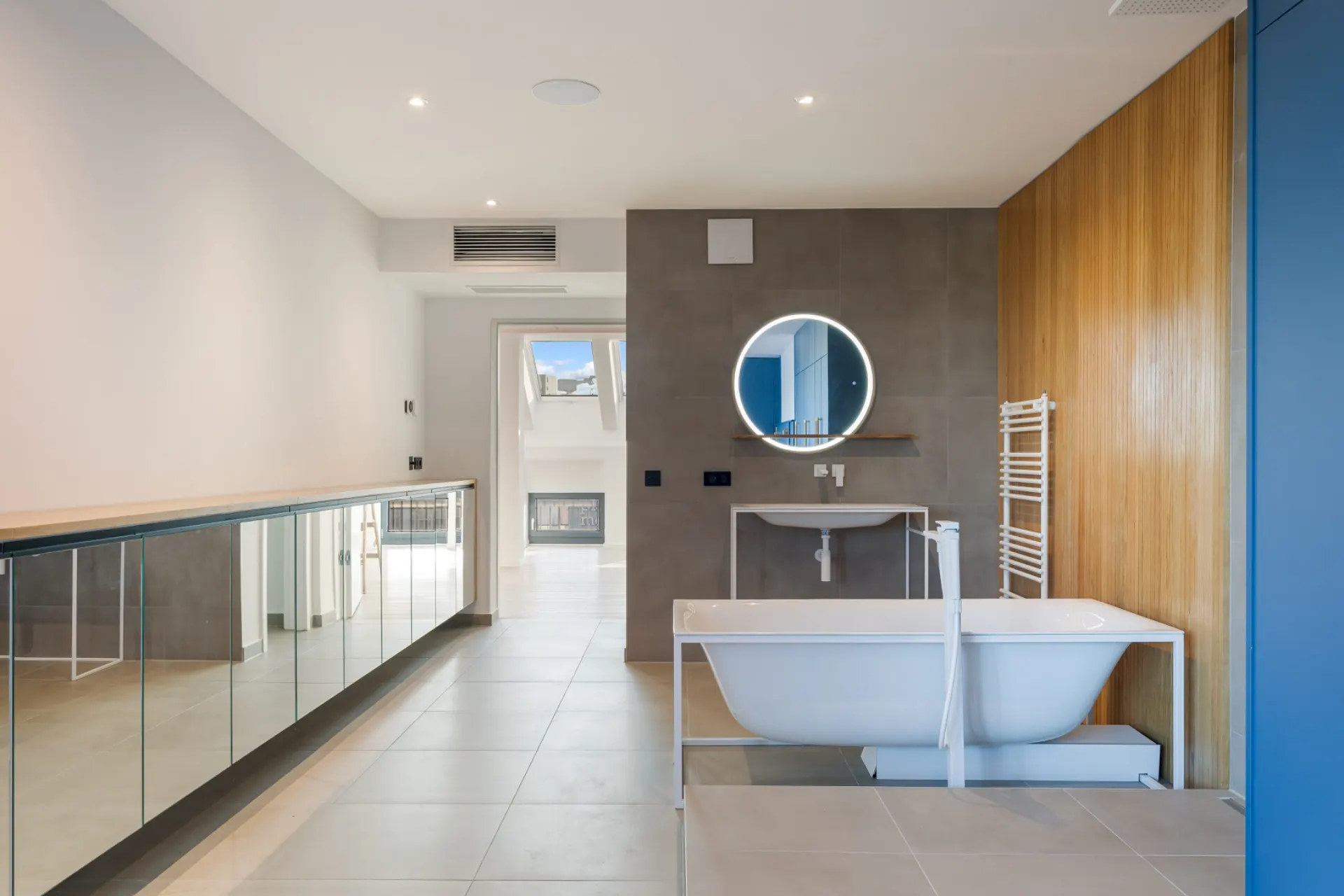 Modernes Badezimmer mit freistehender Badewanne, rundem Spiegel und Holzwand.