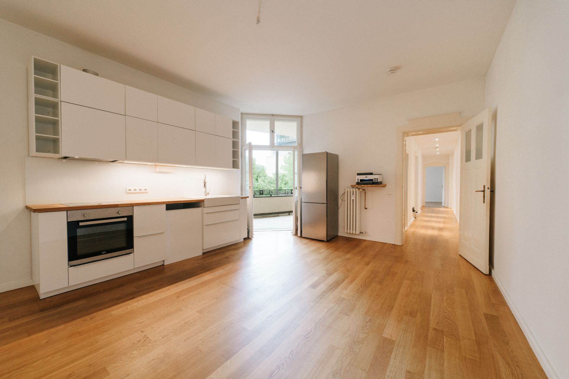 Helle Küche mit weißen Schränken, Holzfußboden und Zugang zu einem Balkon.