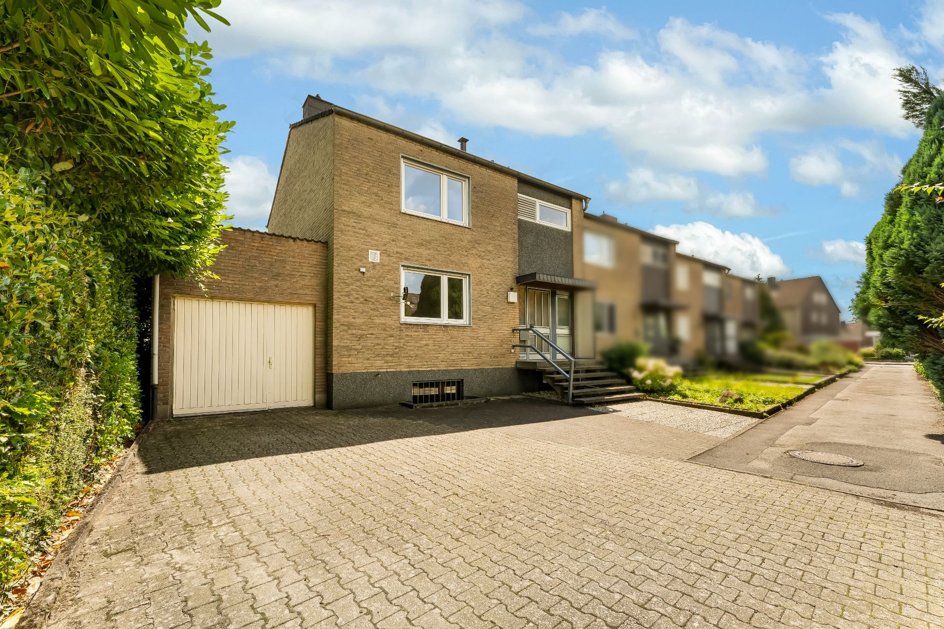 Zweistöckiges Einfamilienhaus mit Garage und gepflasterter Einfahrt in einer Wohnstraße.