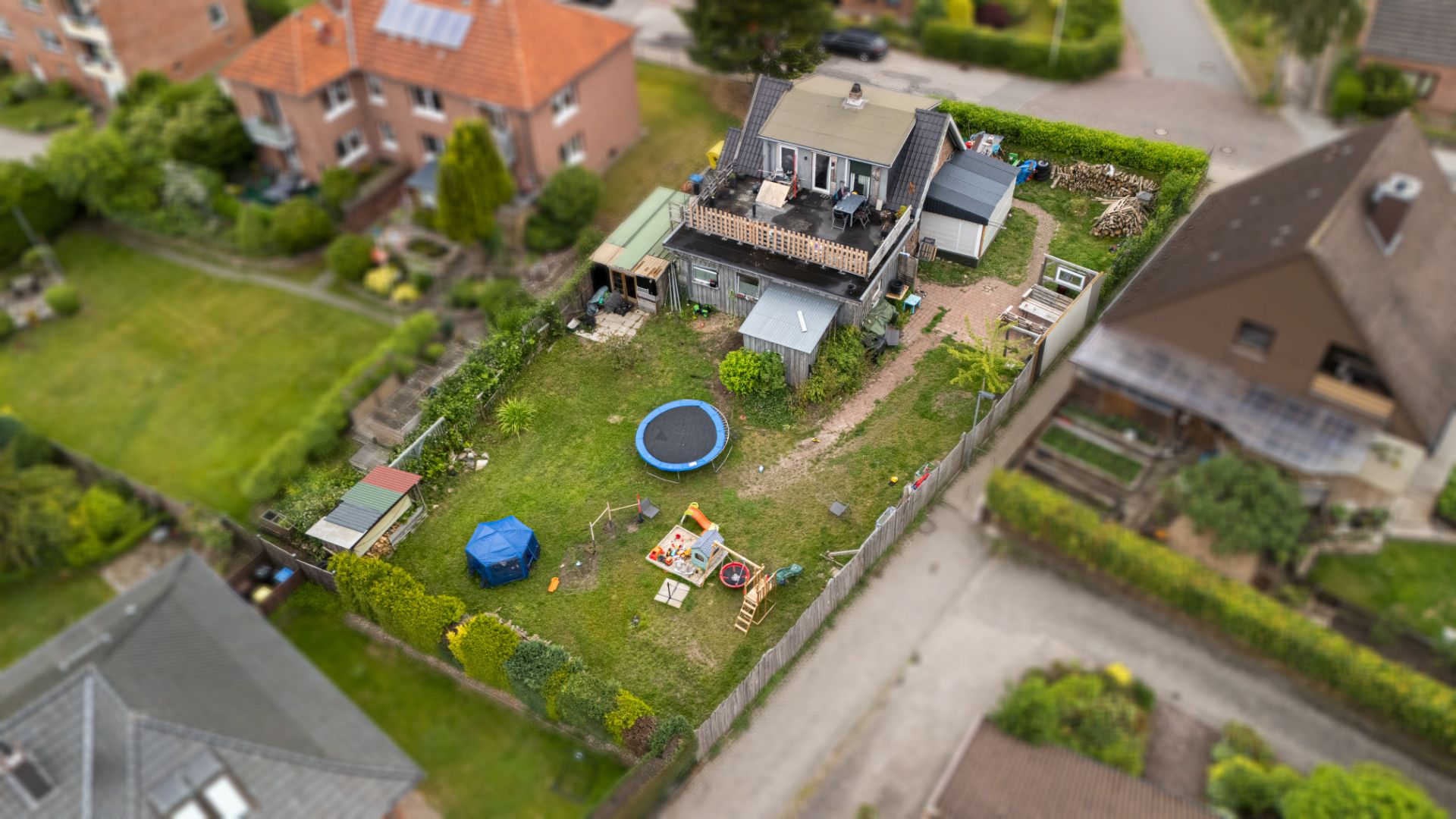 Luftaufnahme eines Gartens mit Haus, Pool, Spielplatz und Terrasse, umgeben von Nachbarhäusern.