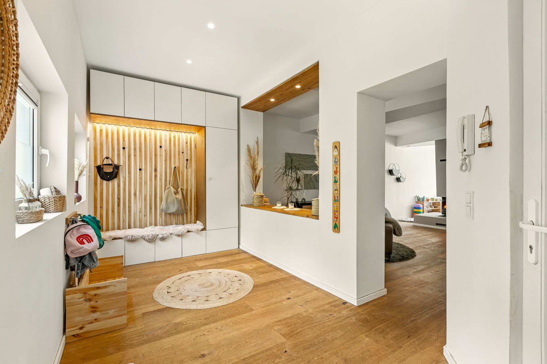 Heller Flur mit Holzfußboden, Sitzbank, Garderobe und Blick ins Wohnzimmer.