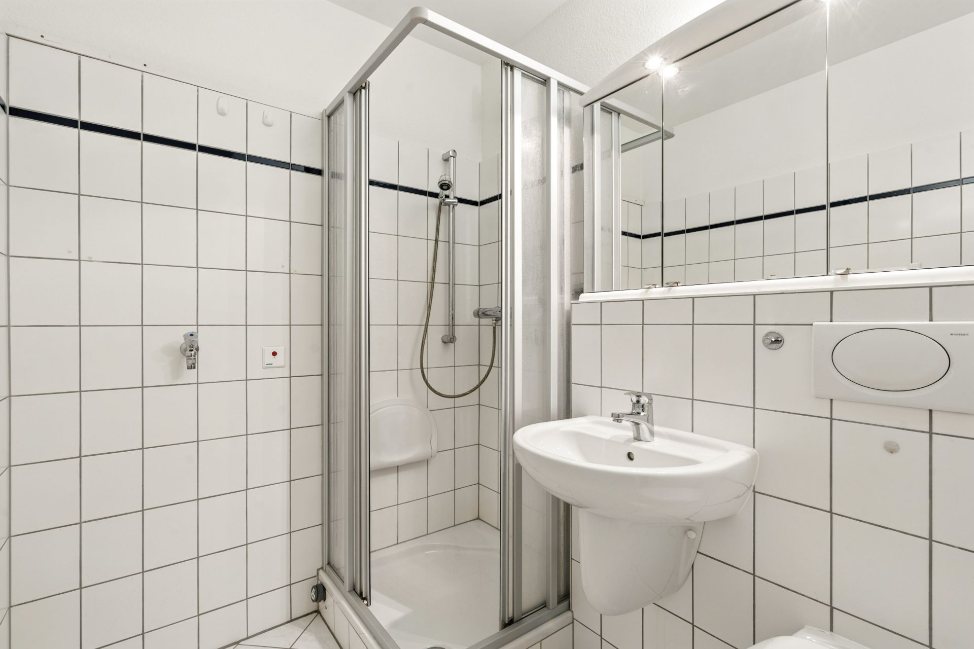 Kleines Badezimmer mit Dusche, Waschbecken und Toilette, weiß gefliest.