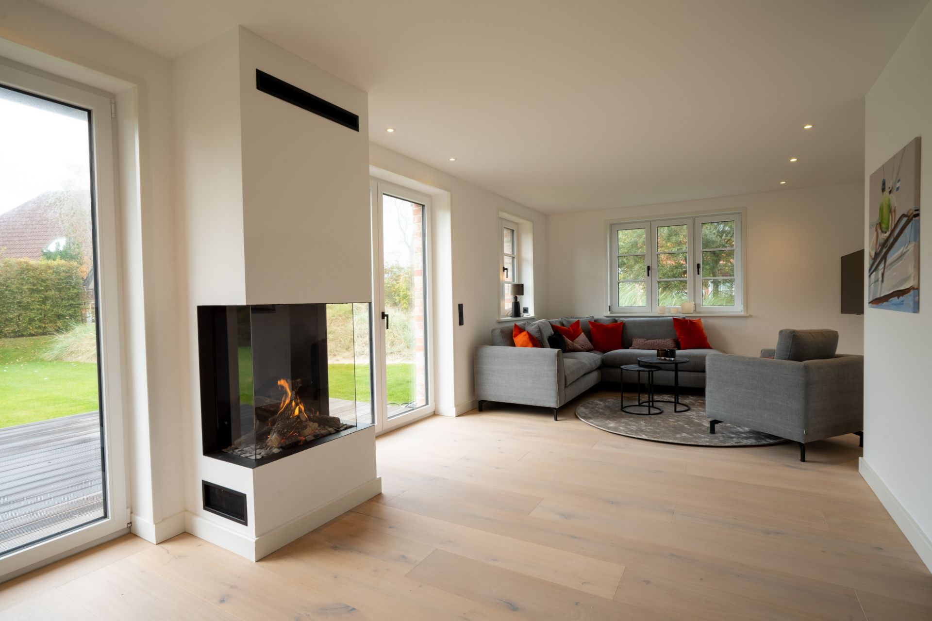 Helles Wohnzimmer mit Kamin, Ecksofa und großen Fenstern mit Blick auf den Garten.