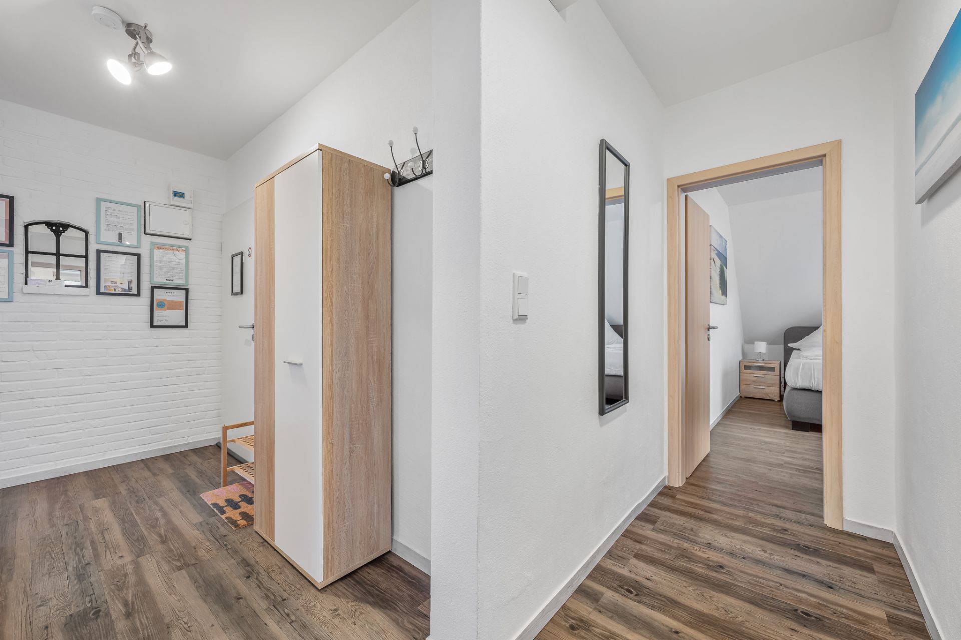 Flur mit Holzfußboden, Schrank, Garderobenhaken und Blick in ein Schlafzimmer.