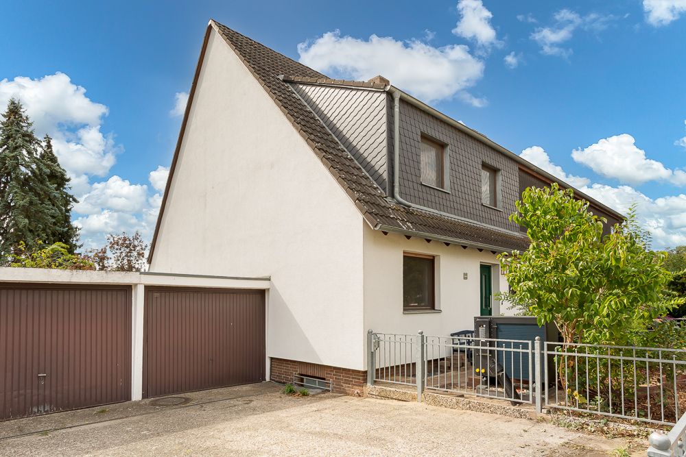 Zweistöckiges Wohnhaus mit Garage und kleinem Vorgarten, umgeben von einem Zaun.