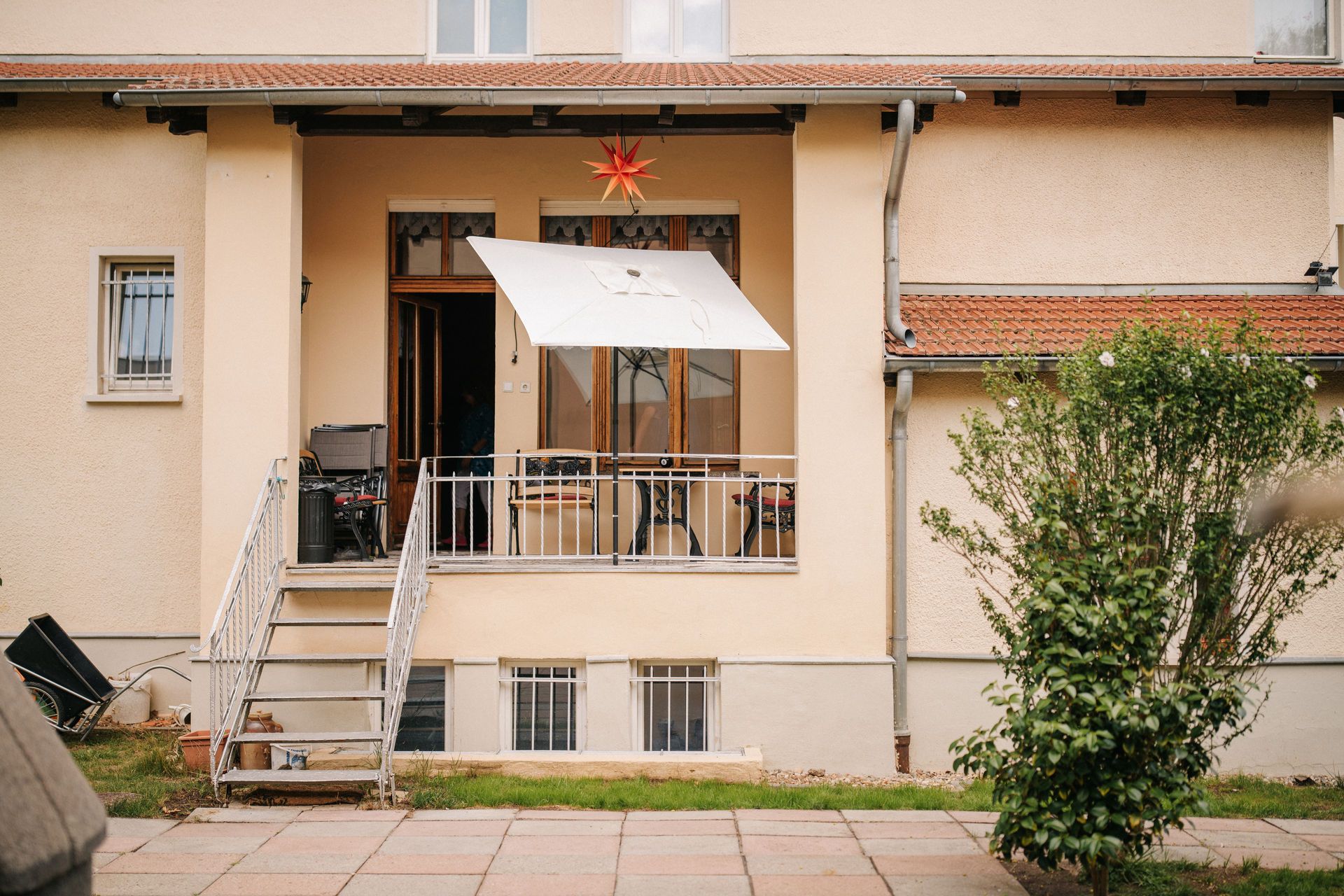 Kleiner Balkon mit weißem Sonnenschirm, Treppe und Garten vor einem Wohnhaus.