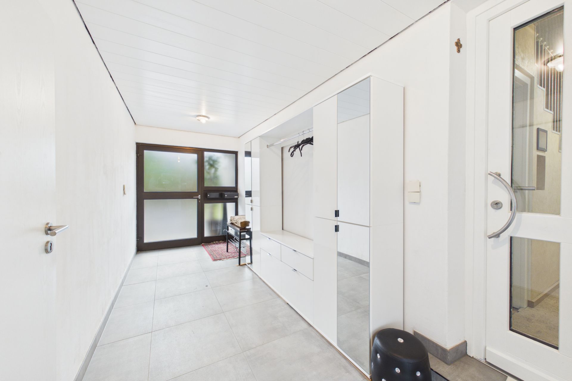 Heller Flur mit Garderobe, Spiegel, Haken und Glastür in einem Wohnhaus.