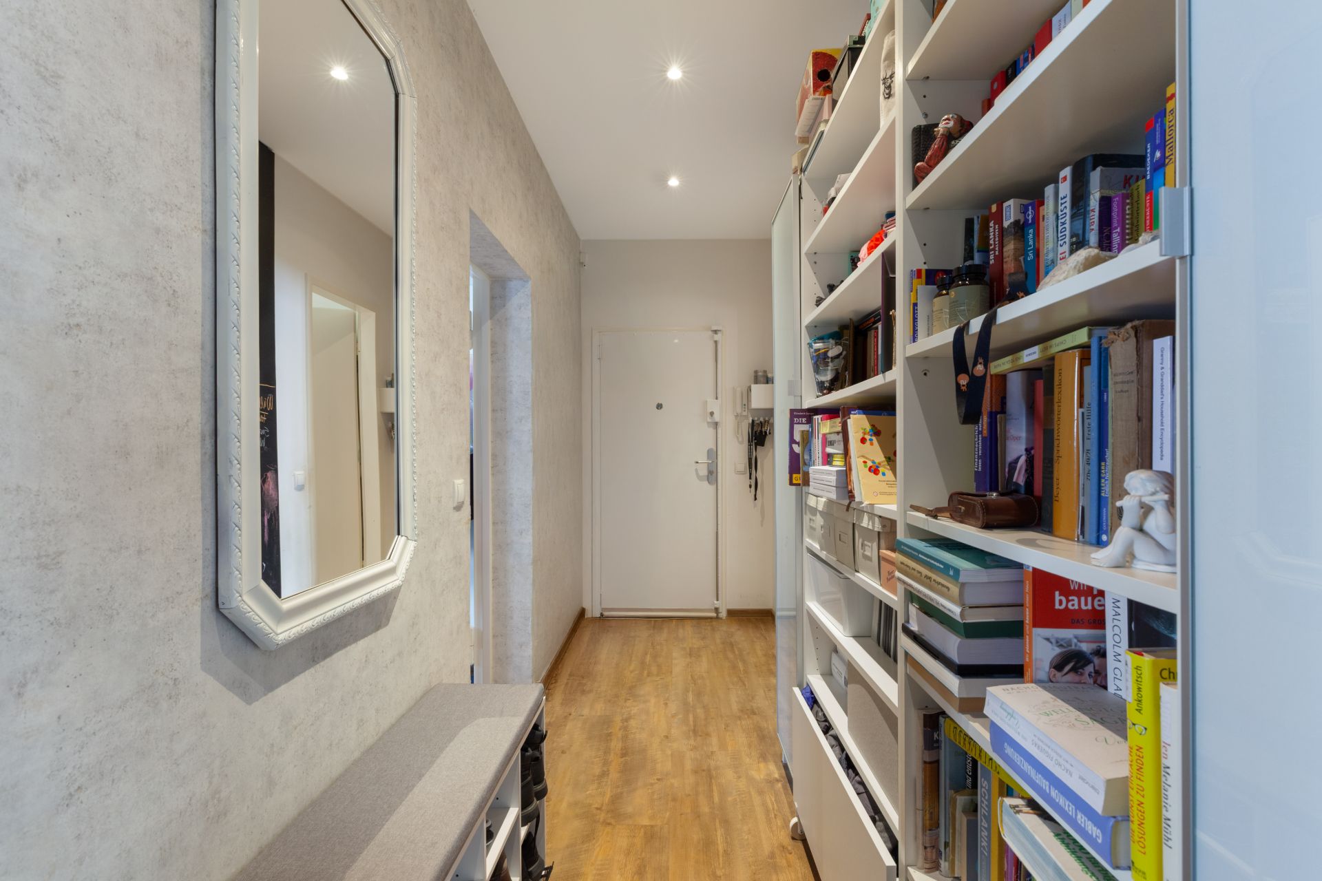 Heller Flur mit Holzfußboden, Spiegel, Regal voller Bücher und Eingangstür.