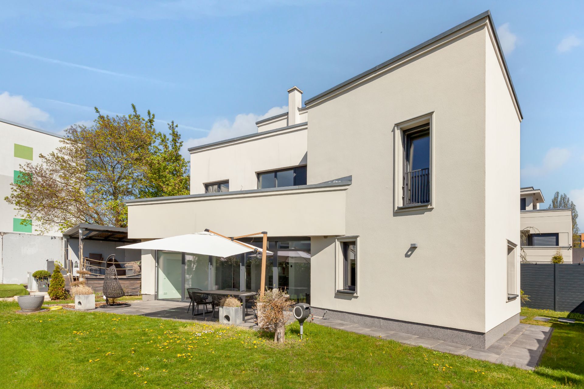 Modernes weißes Wohnhaus mit Terrasse, Sonnenschirm und Garten im Vordergrund.