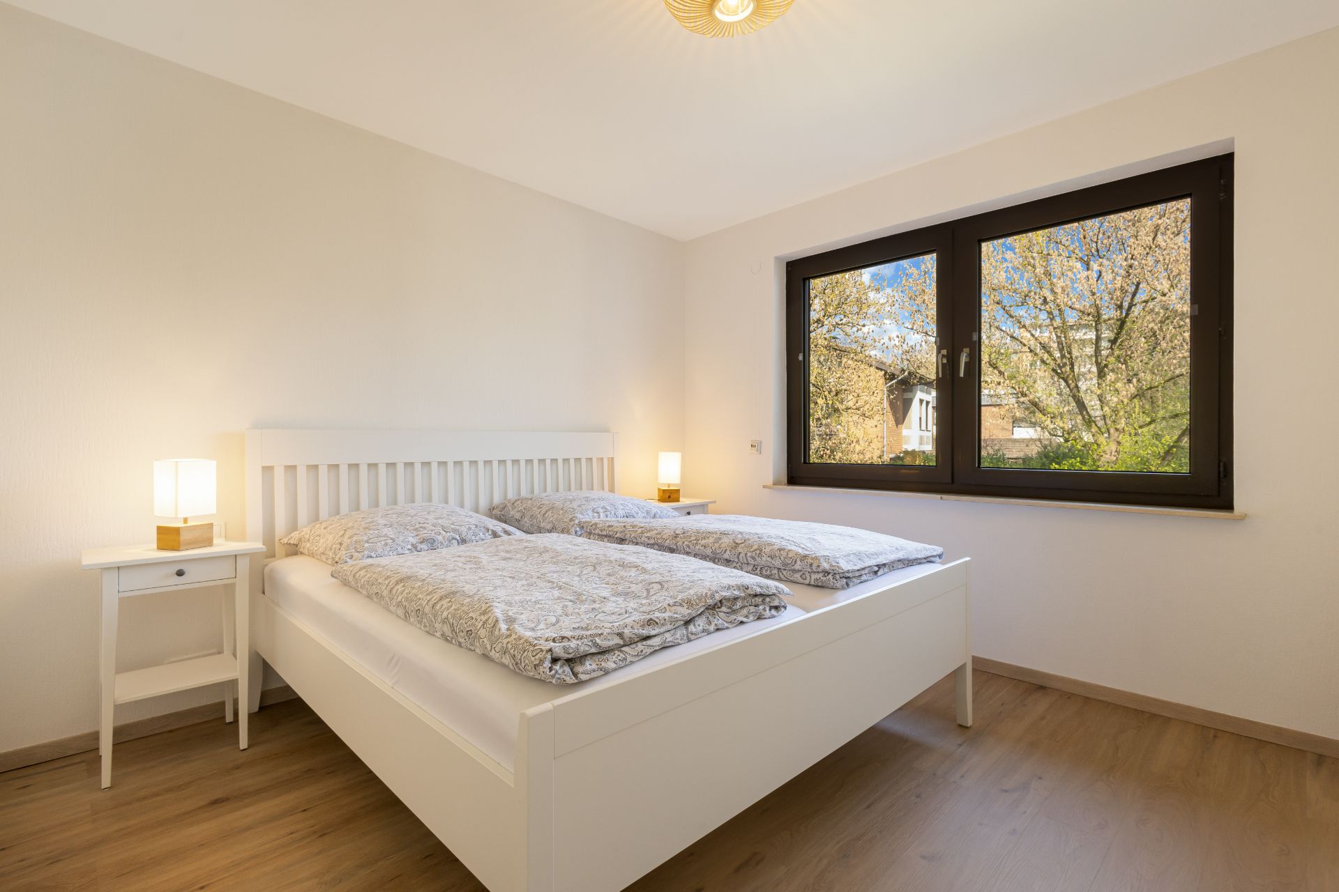 Helles Schlafzimmer mit Doppelbett, zwei Nachttischen und großem Fenster.
