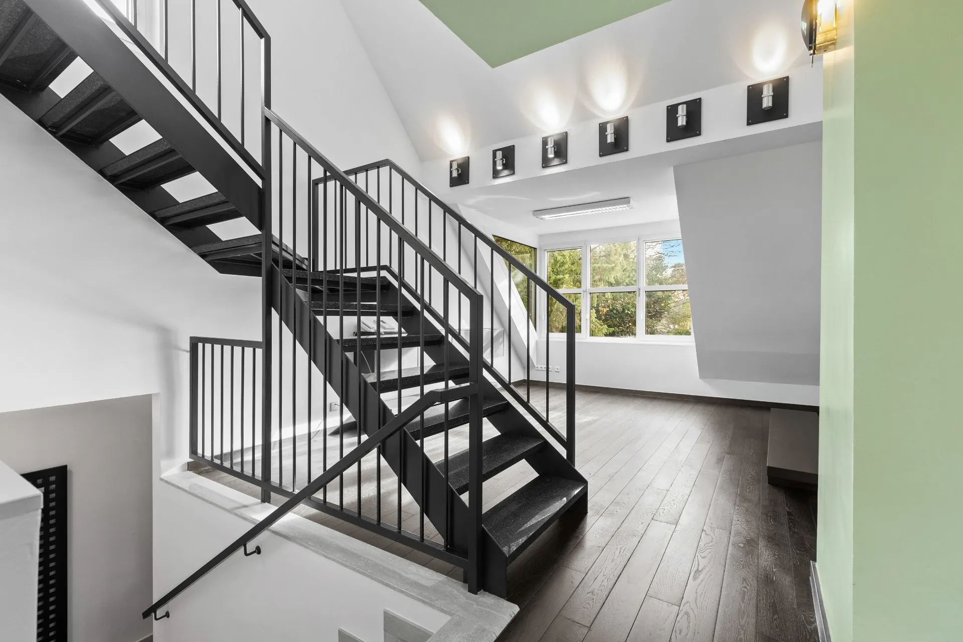Moderner Flur mit schwarzer Treppe, Holzfußboden und großen Fenstern mit Blick ins Grüne.