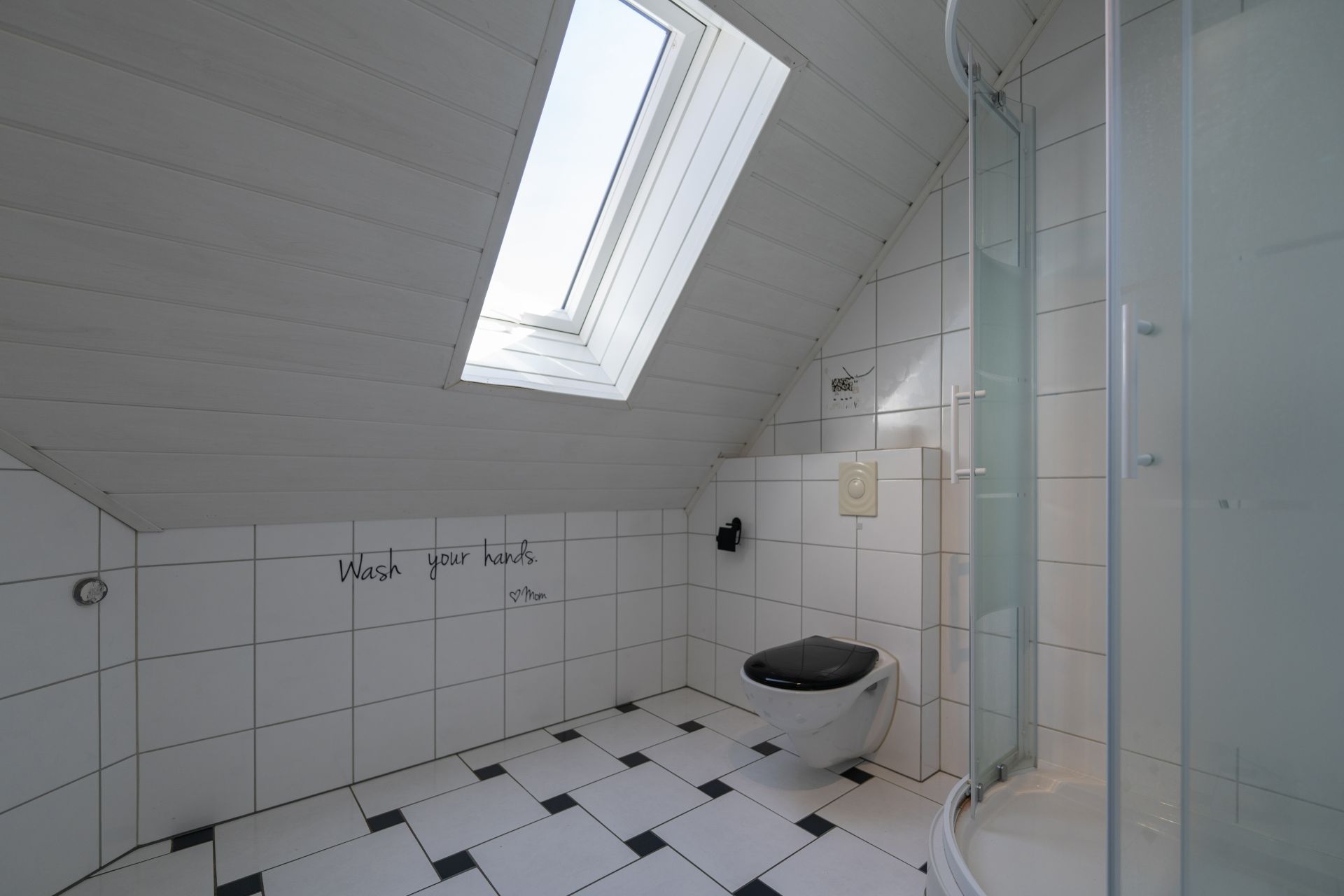 Modernes weiß gefliestes Bad mit Dachfenster, Toilette und runder Duschkabine.