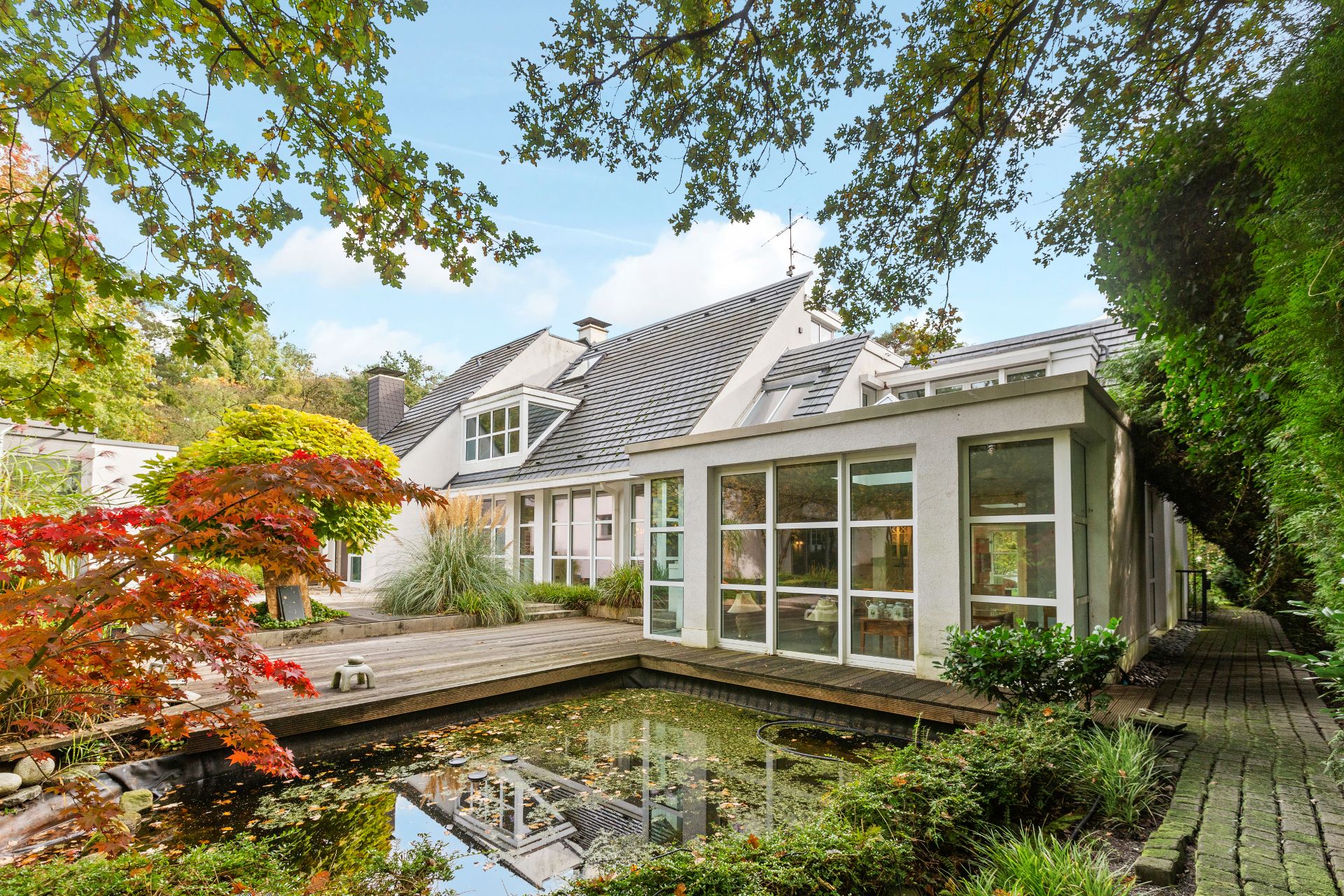 Modernes Wohnhaus mit Wintergarten, Holzterrasse und kleinem Teich im Garten.