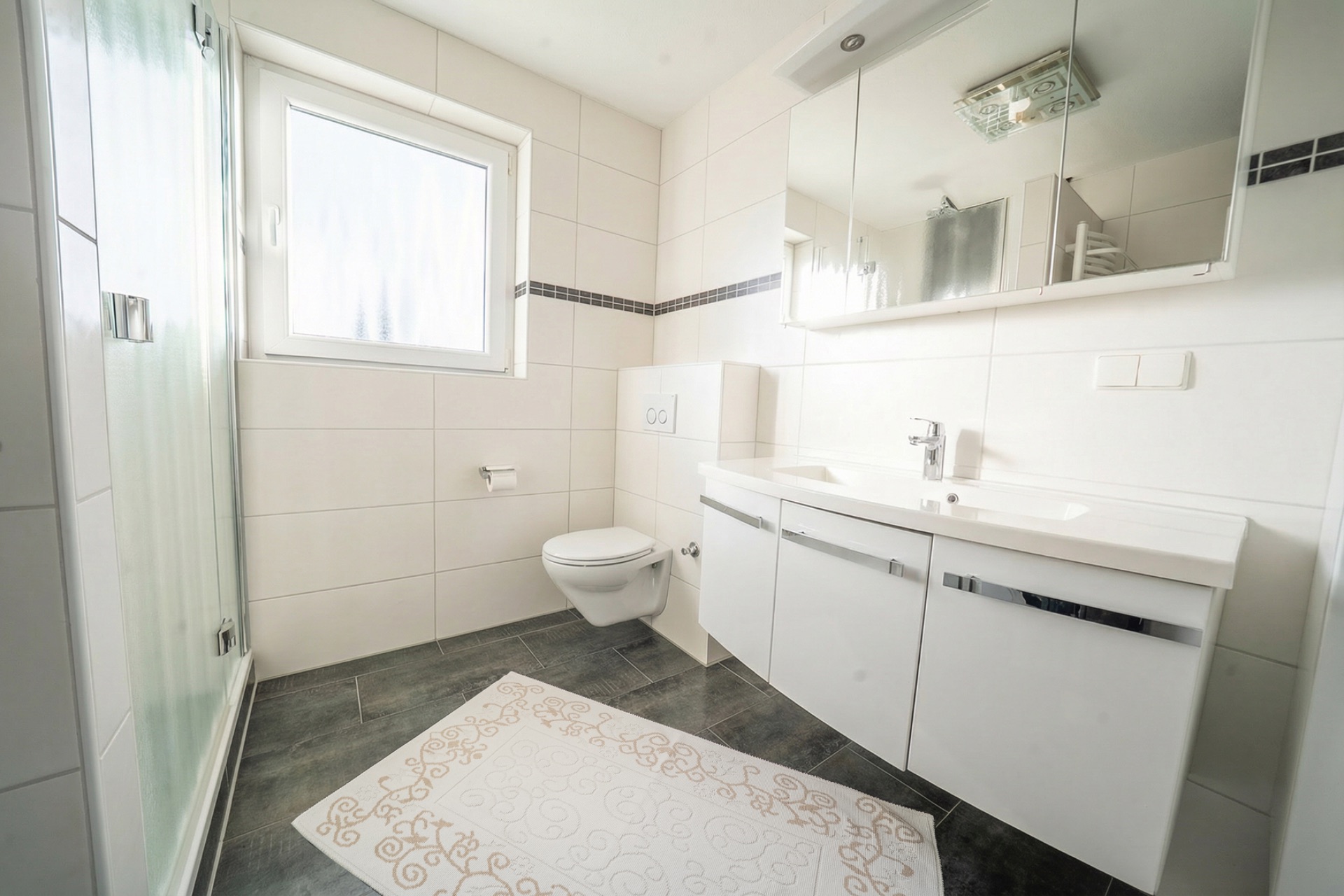Modernes Badezimmer mit Dusche, Fenster, Wandtoilette, Doppelwaschbecken und Spiegel.