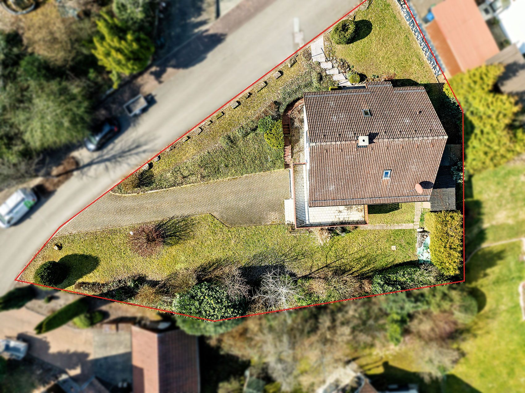 Luftaufnahme eines Einfamilienhauses mit Garten, das von einer roten Linie umrandet ist.