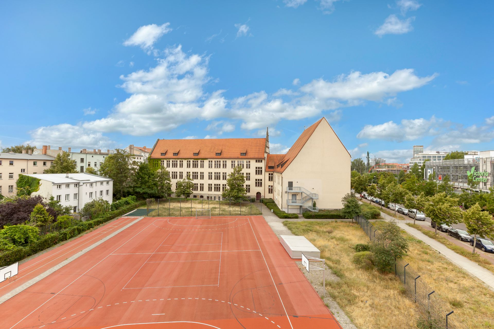 Großer roter Sportplatz mit Basketball- und Fußballtoren neben einem Gebäude mit rotem Dach.