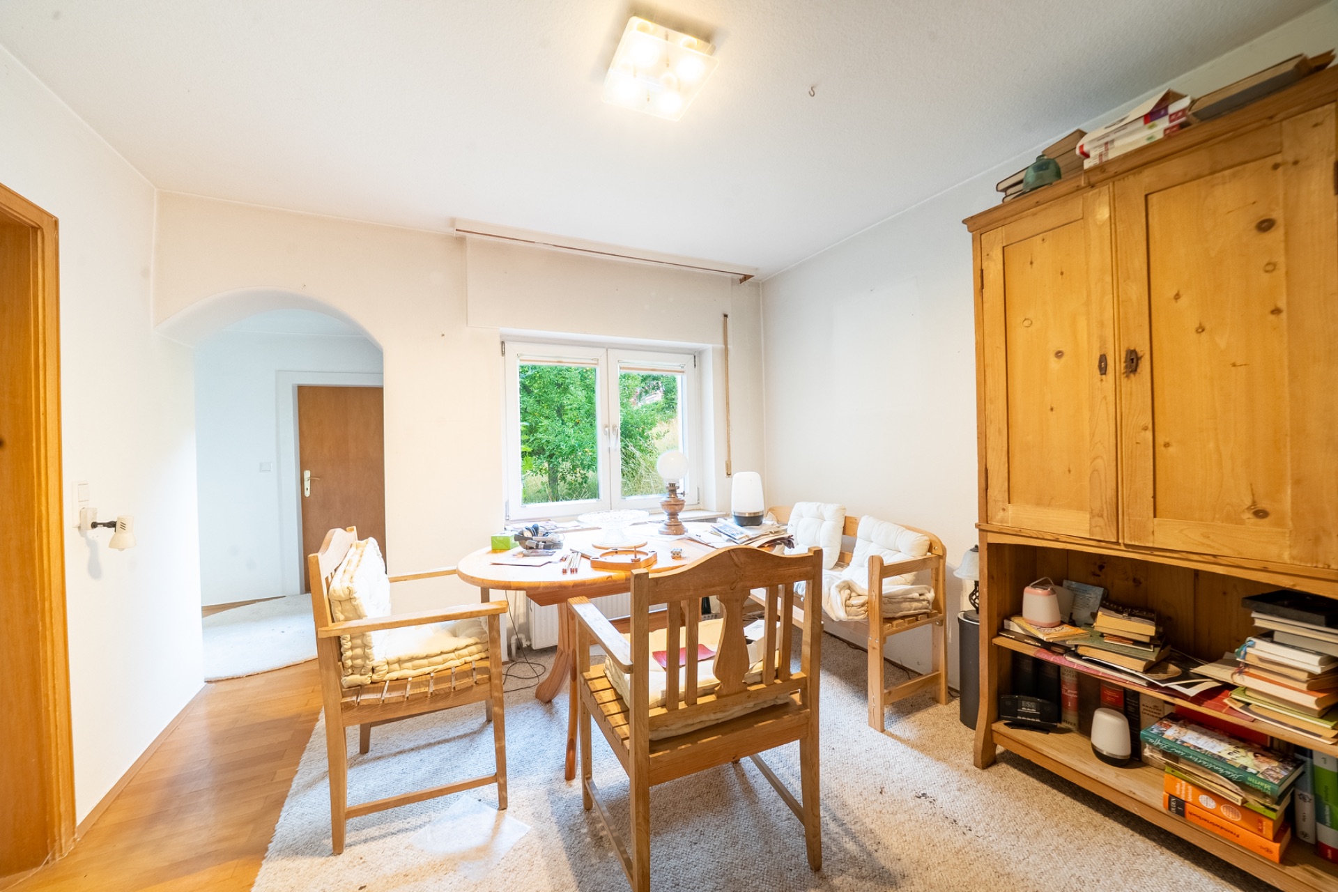 Wohnzimmer mit Holzmöbeln, Esstisch, Stühlen, Sofa und einem Fenster mit Blick ins Grüne.