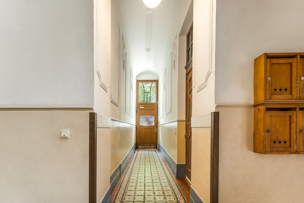 Heller Flur mit gemustertem Fliesenboden, Holztür und Holzbriefkästen an der Wand.