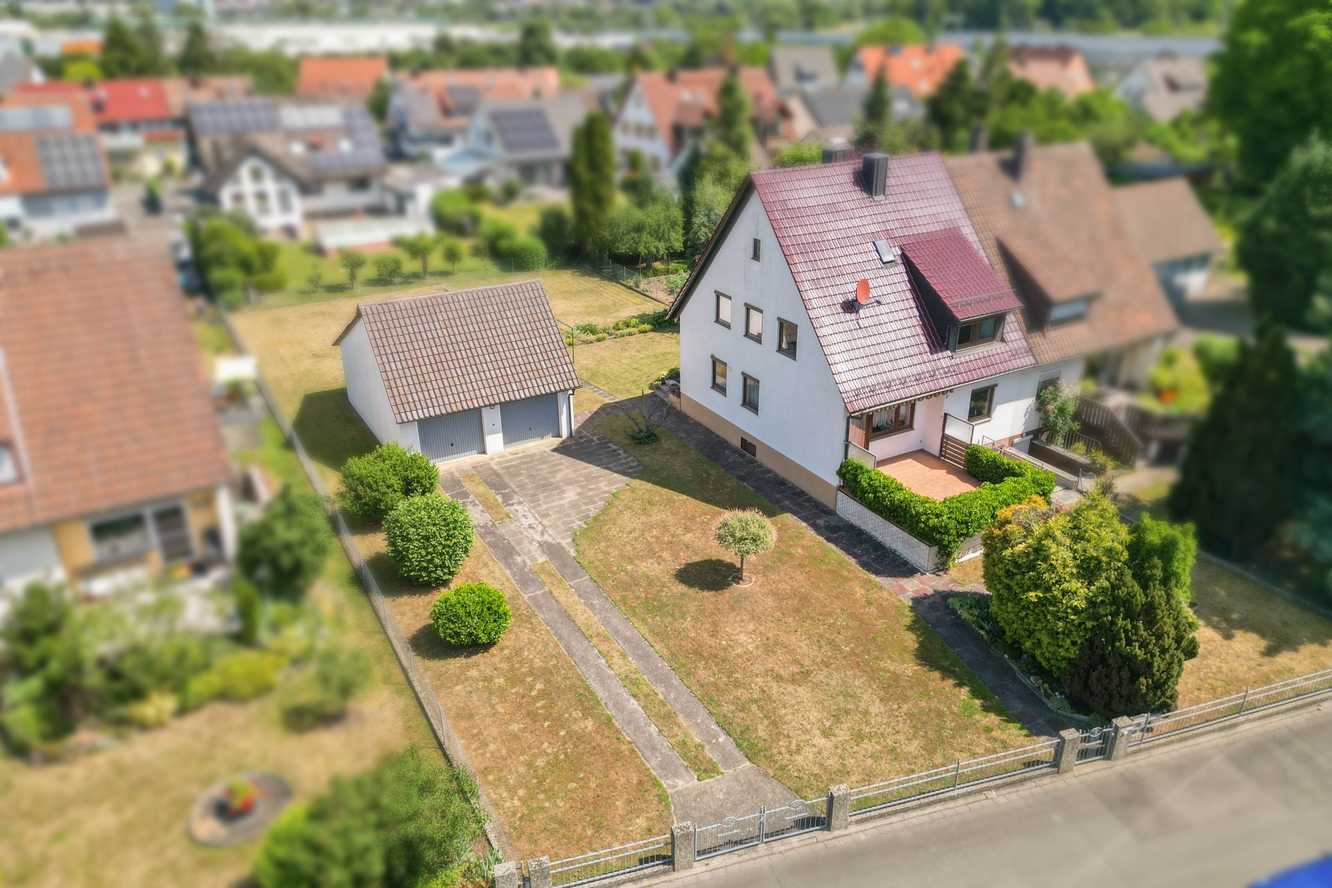 Luftaufnahme eines Einfamilienhauses mit Garten, Einfahrt und separater Garage.