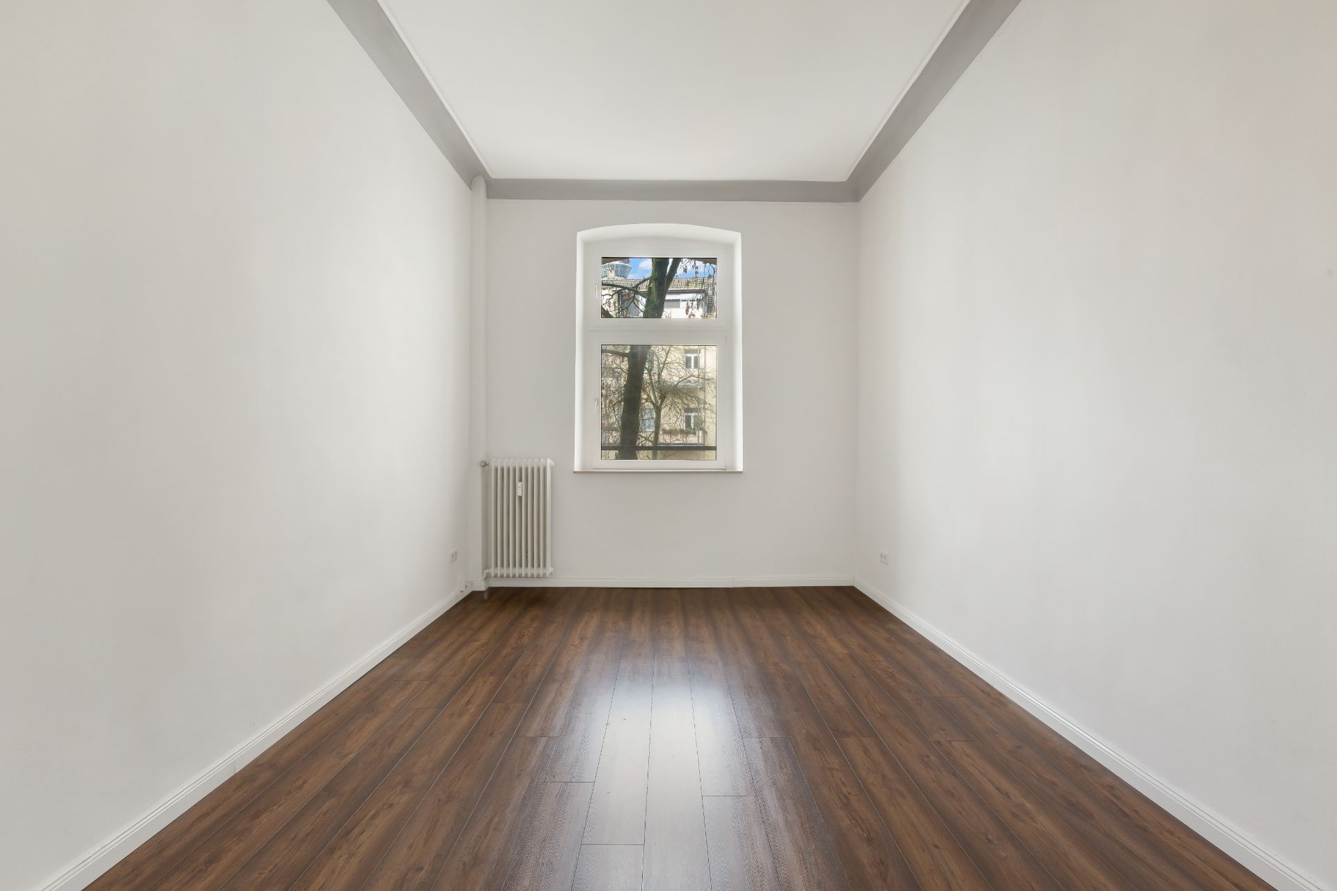 Leerer Raum mit weiß gestrichenen Wänden, Holzfußboden und einem Fenster mit Blick nach draußen.