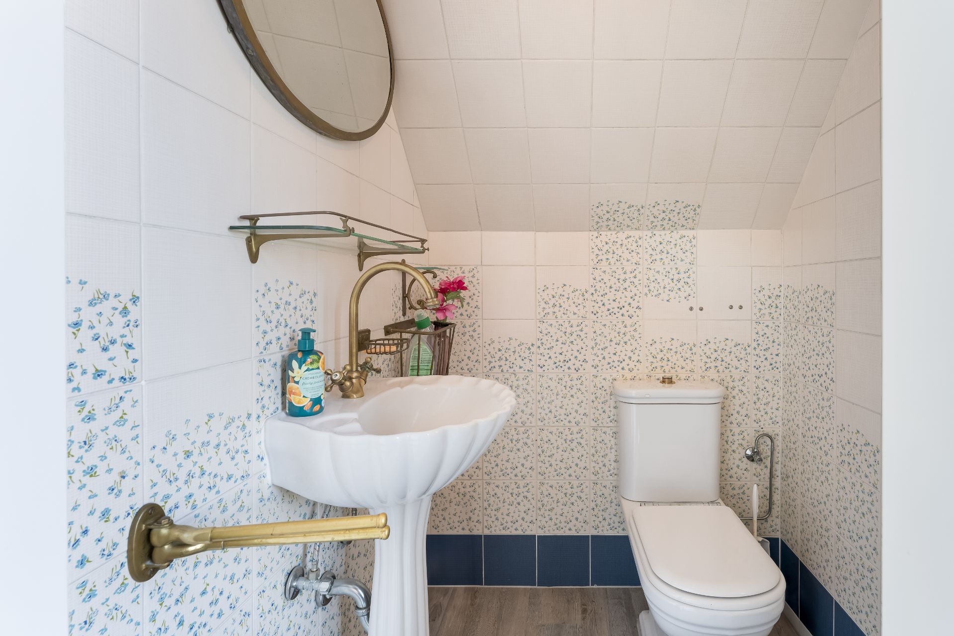 Kleines Badezimmer mit Waschbecken, Spiegel, Toilette und weiß-blauen Fliesen.