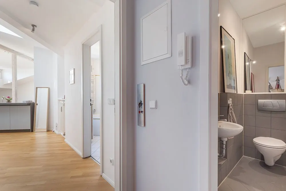 Flur mit Blick auf ein Badezimmer und Wohnzimmer, Holzboden und Wandtelefon sichtbar.
