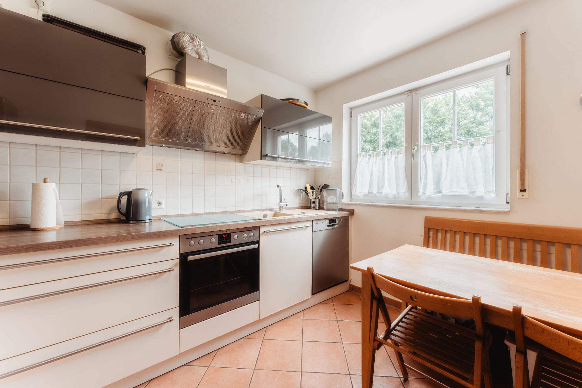 Moderne Küche mit Herd, Spüle, Geschirrspüler, Esstisch und Fenster mit Vorhängen.