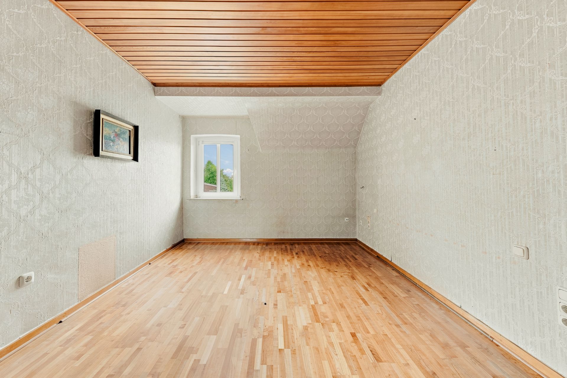Leerer Raum mit Holzfußboden, Holzdecke, weißem Fenster und Bild an der Wand.