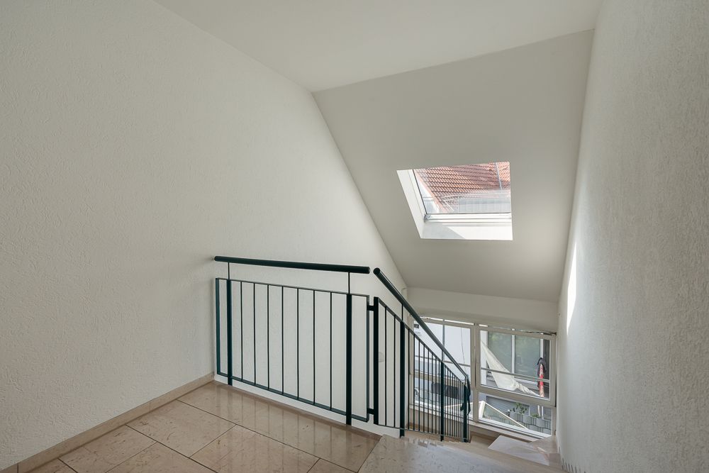 Helles Treppenhaus mit Dachfenster und Fliesenboden in einem Wohngebäude.