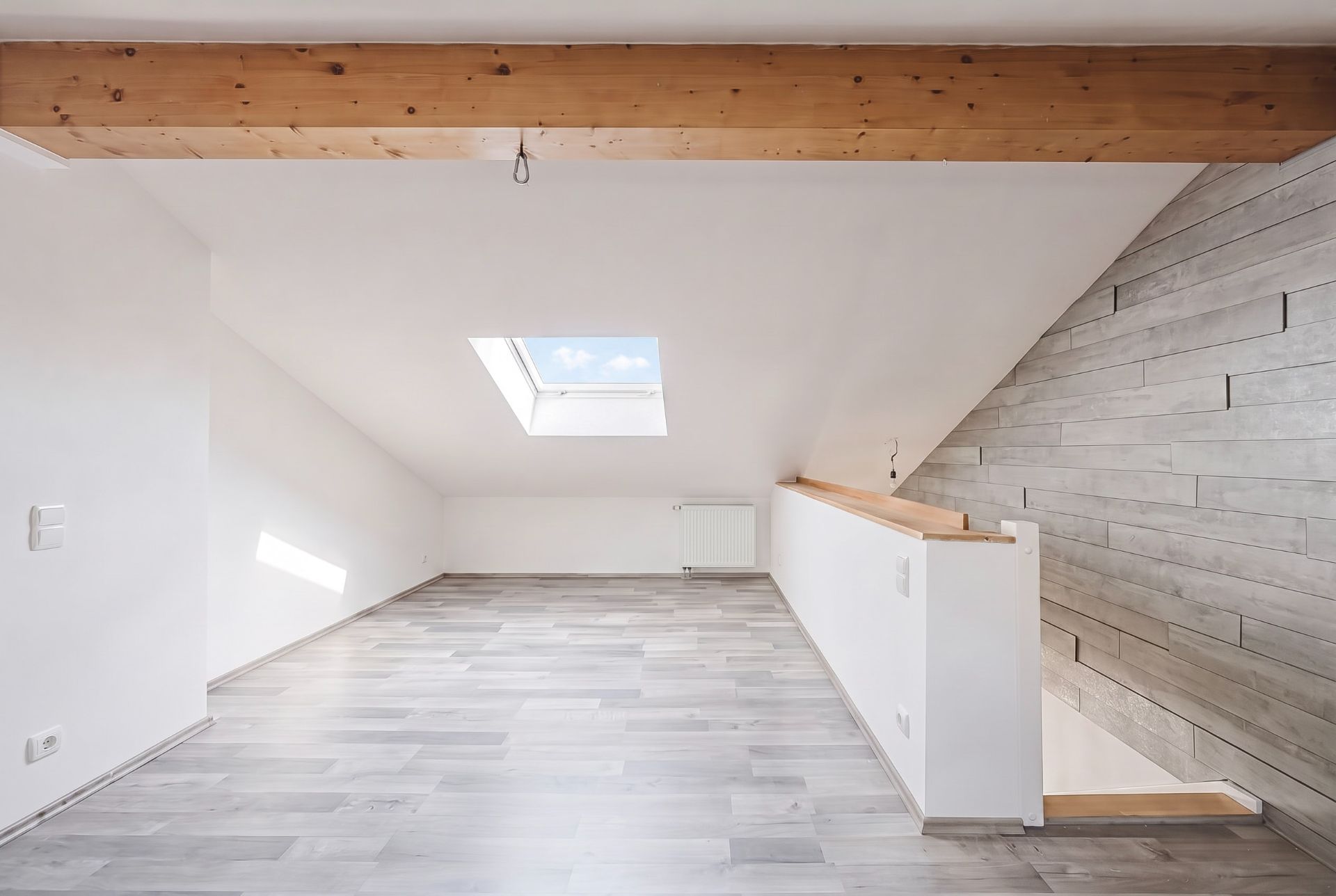 Heller Dachraum mit Holzfußboden, Holzbalken, Dachfenster und Treppe.