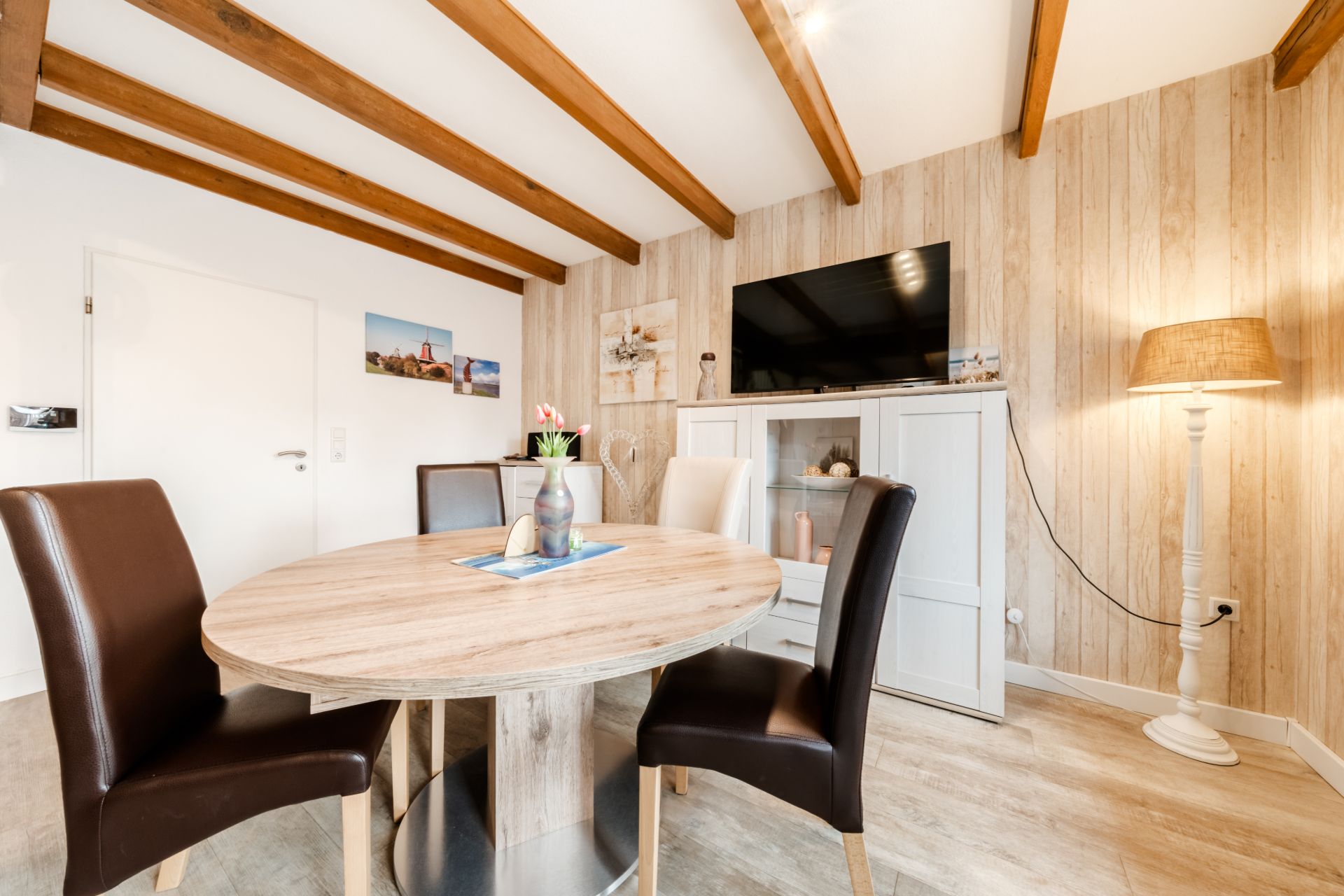 Essbereich mit rundem Tisch, vier Stühlen, Fernseher und Stehlampe in einem hellen Raum.