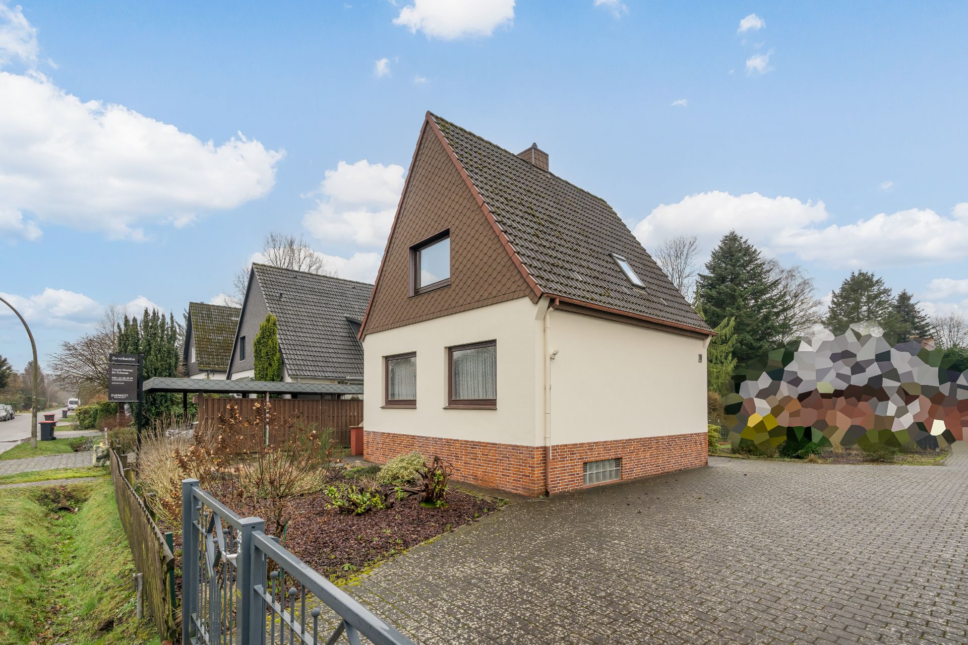 Einfamilienhaus mit Satteldach, gepflasterte Einfahrt und Vorgarten, blauer Himmel.