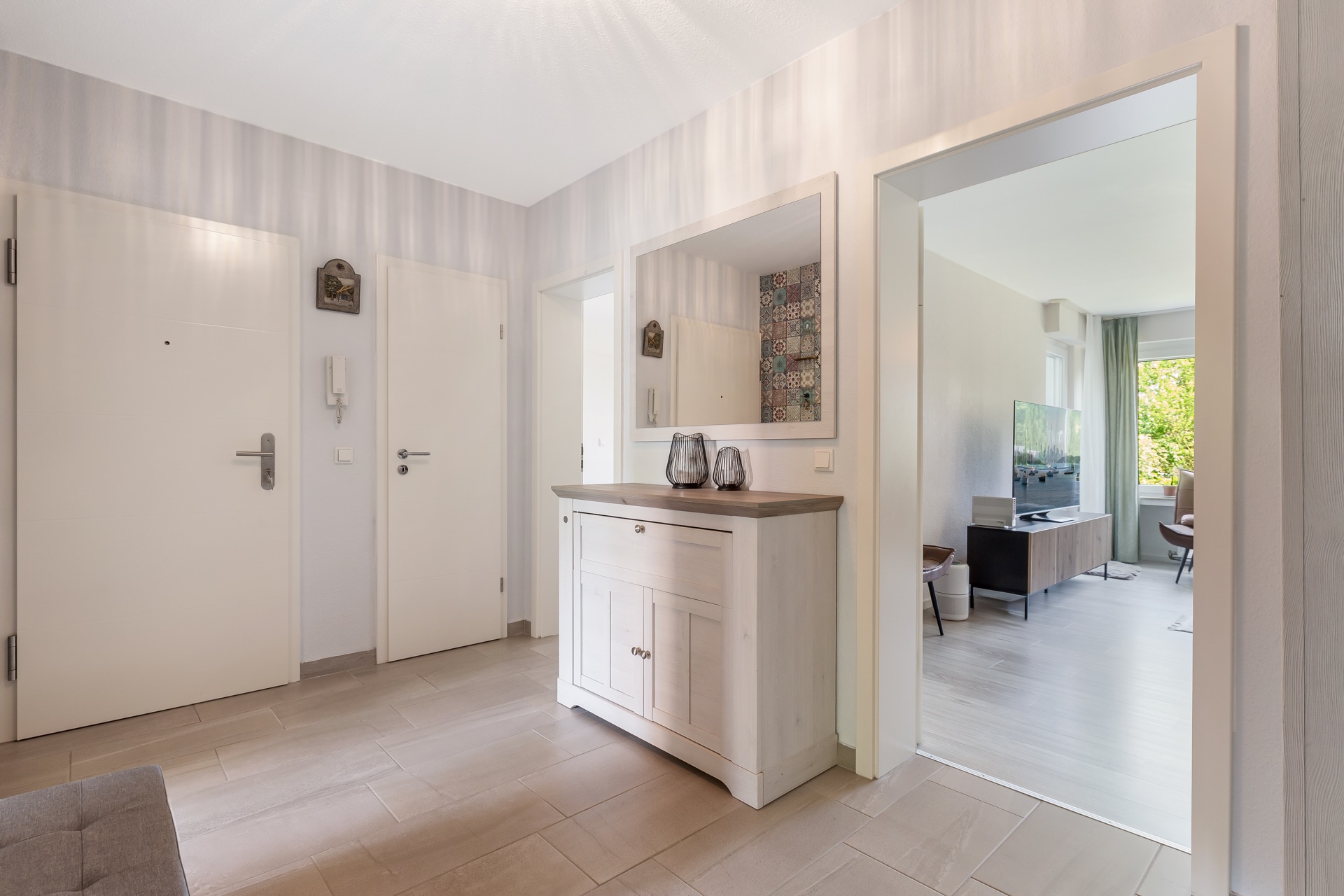 Heller Flur mit Kommode, großem Spiegel und Blick ins Wohnzimmer mit Fernseher.