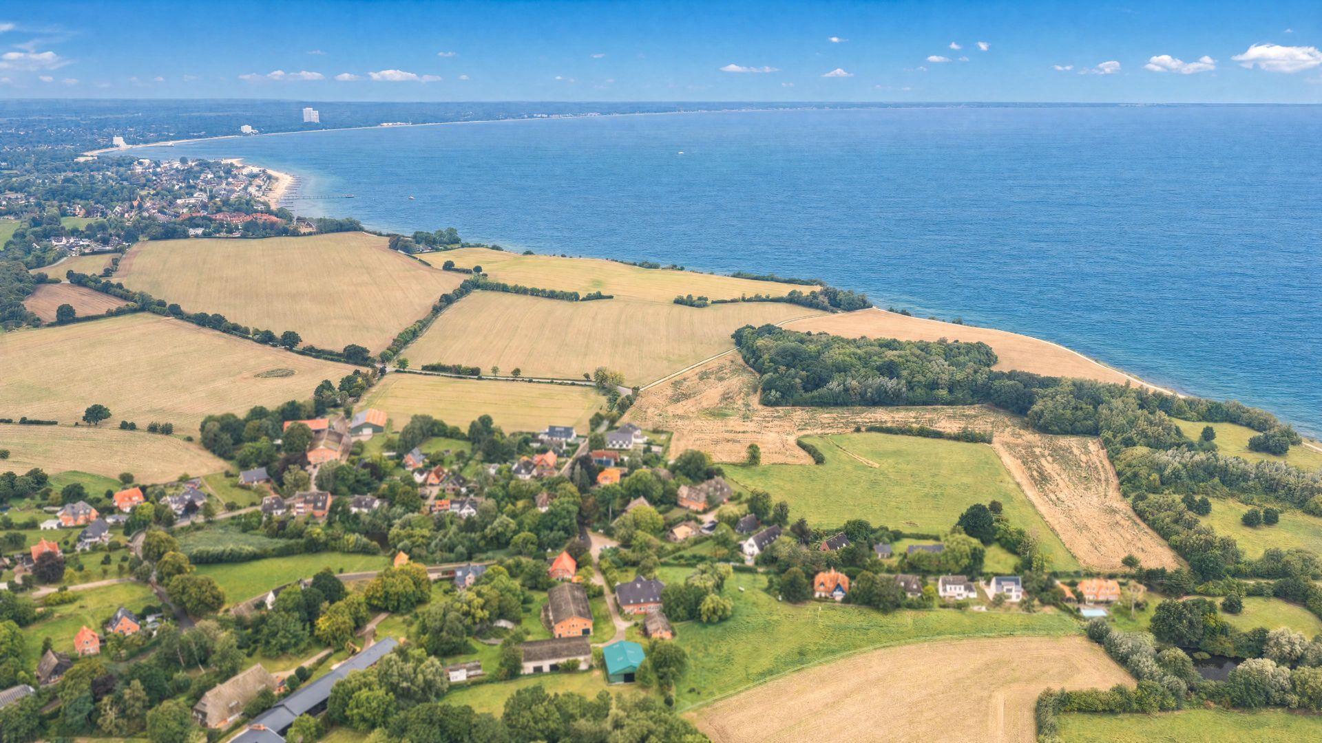 Luftaufnahme von Häusern, Feldern und Küste mit Blick auf das Meer.