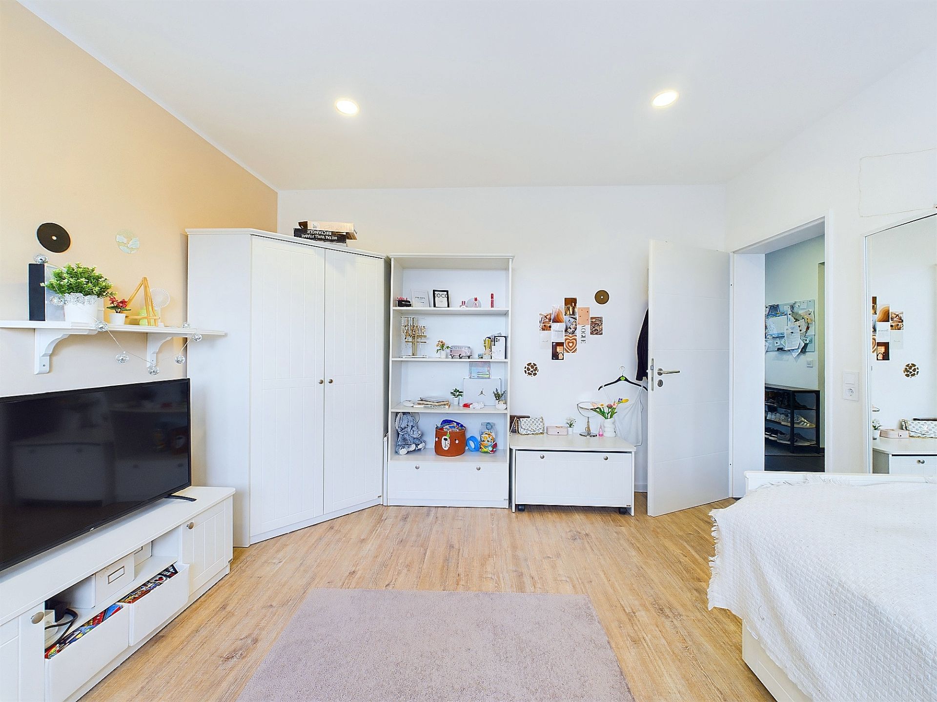 Helles Schlafzimmer mit Fernseher, weißem Regal, Schrank und Dekorationen an der Wand.