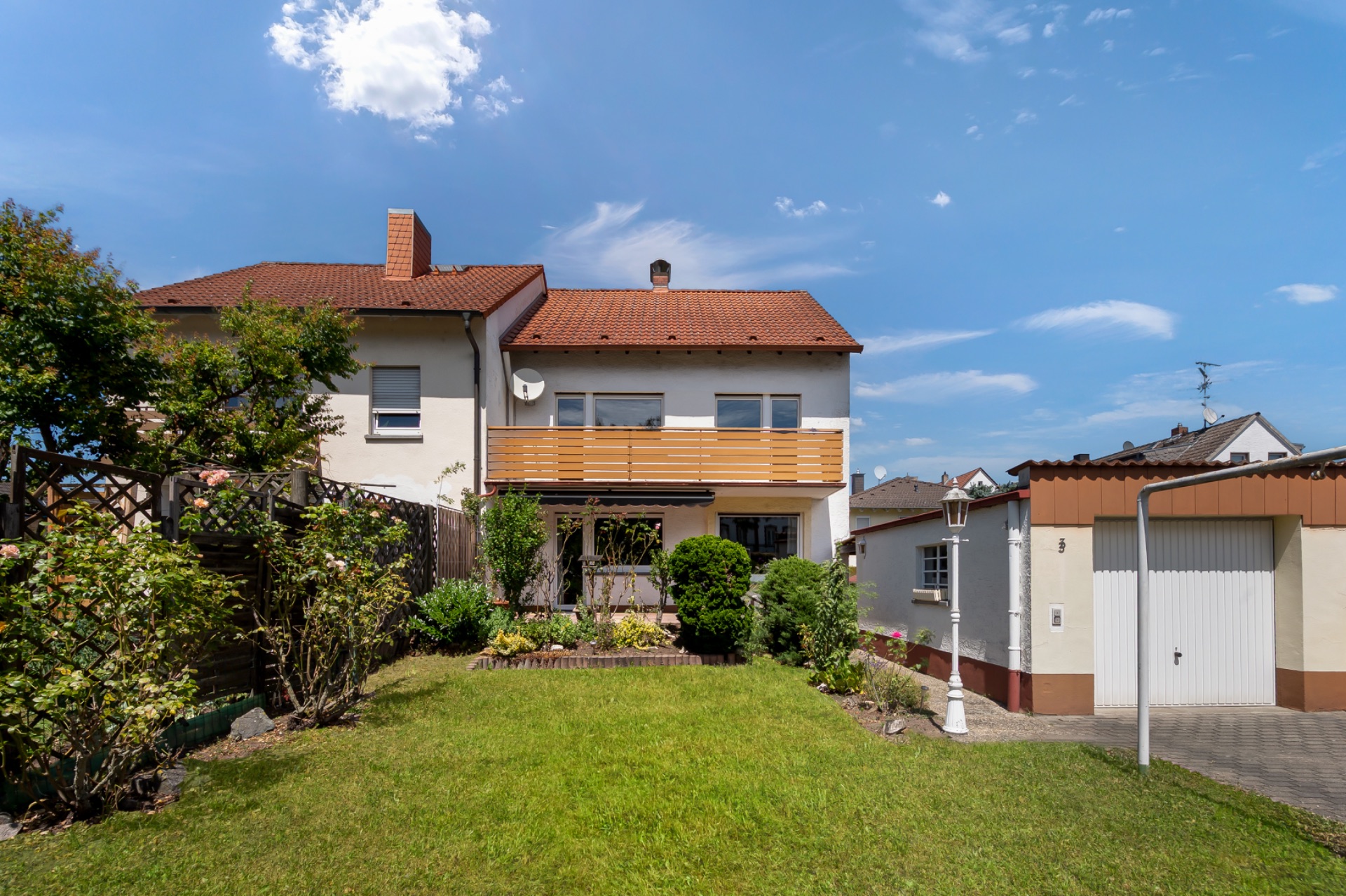 Zweistöckiges Wohnhaus mit Garten, Terrasse und Garage bei sonnigem Wetter.