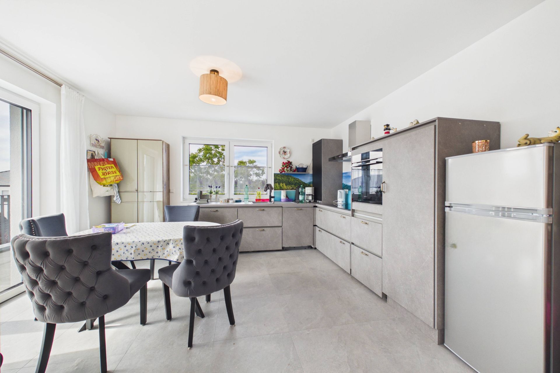 Moderne Küche mit grauen Schränken, Esstisch und gepolsterten Stühlen vor großem Fenster.