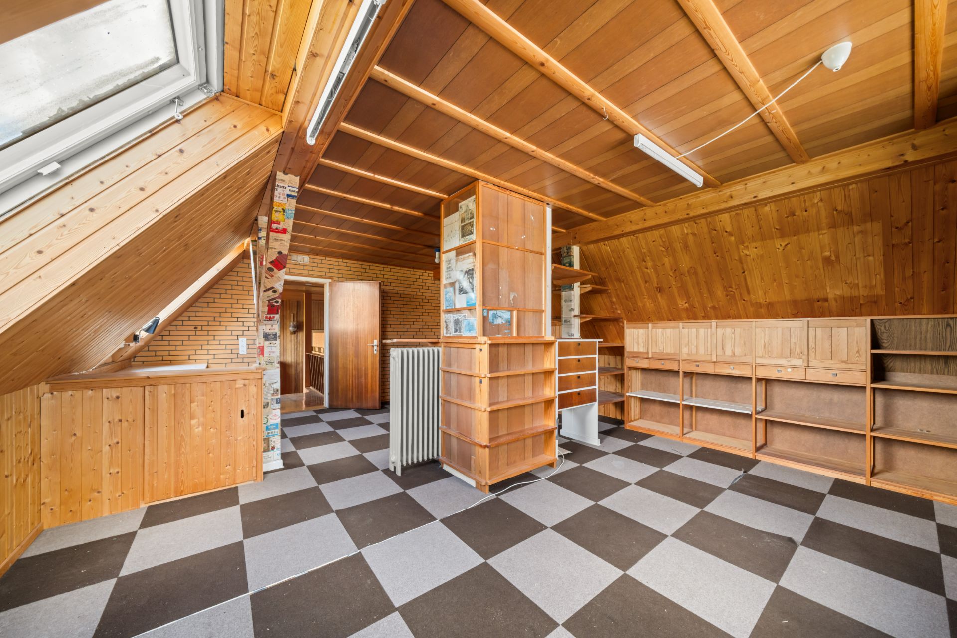 Dachzimmer mit Holzregalen, Schachbrettboden und großem Dachfenster.