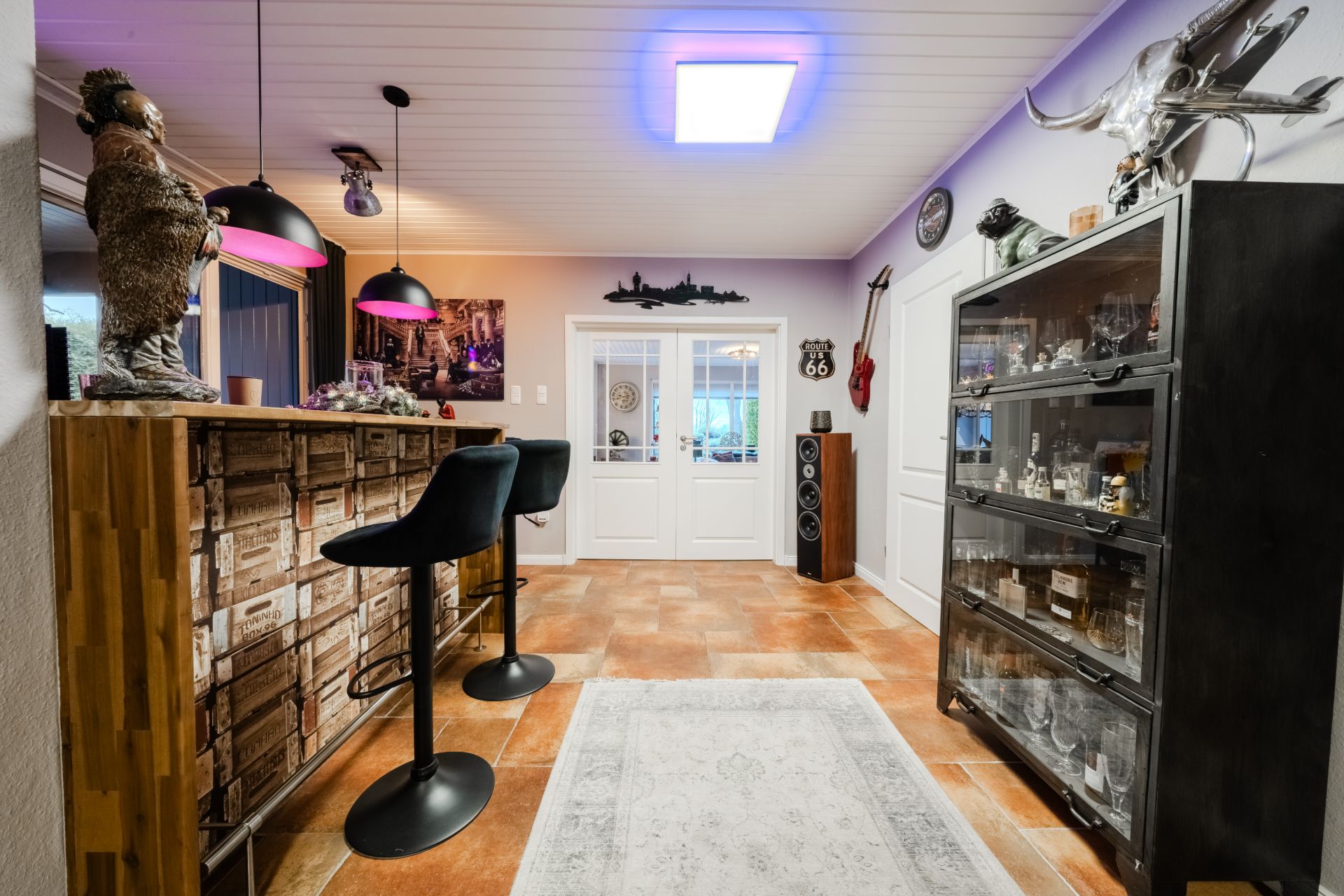 Wohnbereich mit Bartresen, zwei Barhockern, Glasvitrine und Dekorationen an den Wänden.