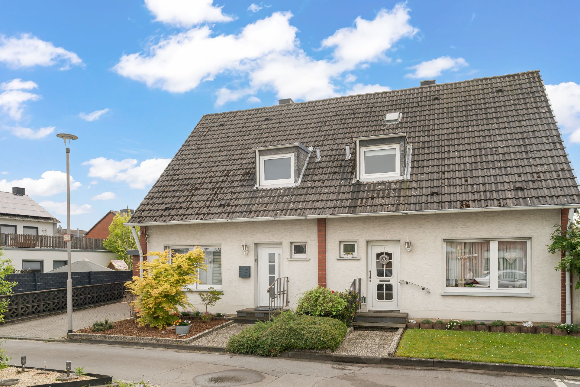 Doppelhaushälfte mit grauem Dach, Vorgarten und zwei Eingängen an einer ruhigen Straße.