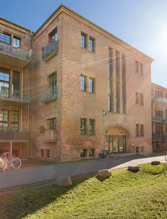 Backstein-Wohngebäude mit Balkonen, Wegen, Bäumen und Fahrrädern bei Sonnenschein.