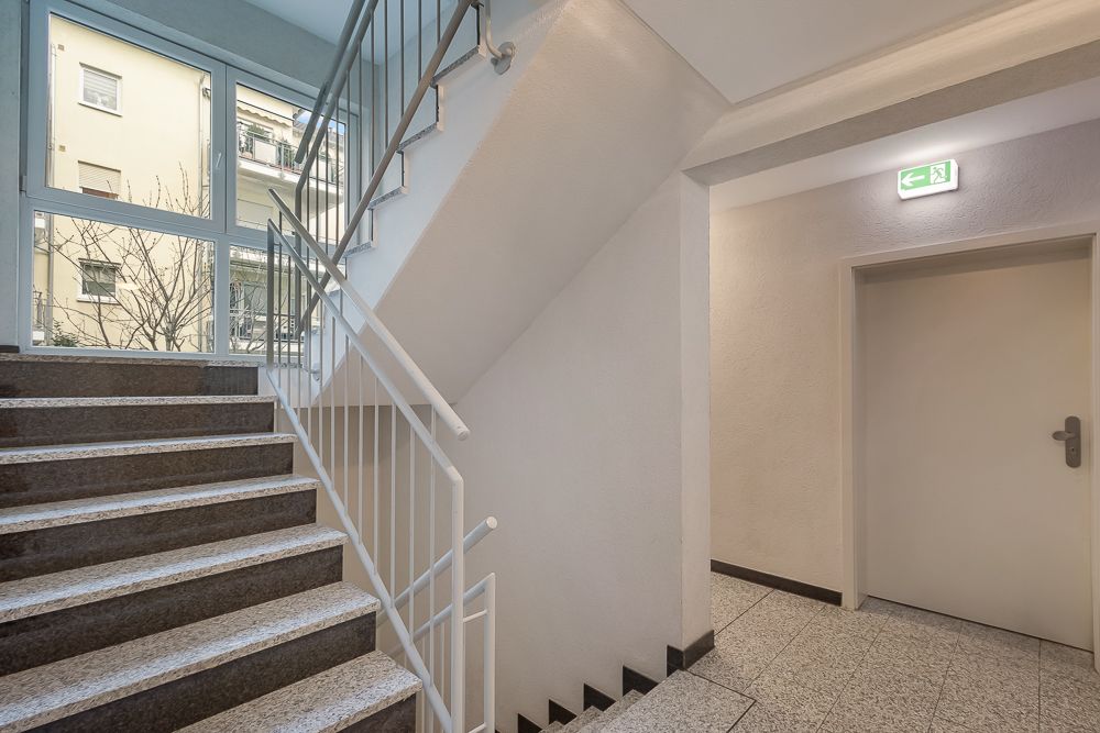 Treppenhaus mit Fenster, Handlauf und einer Tür mit Notausgangsschild.