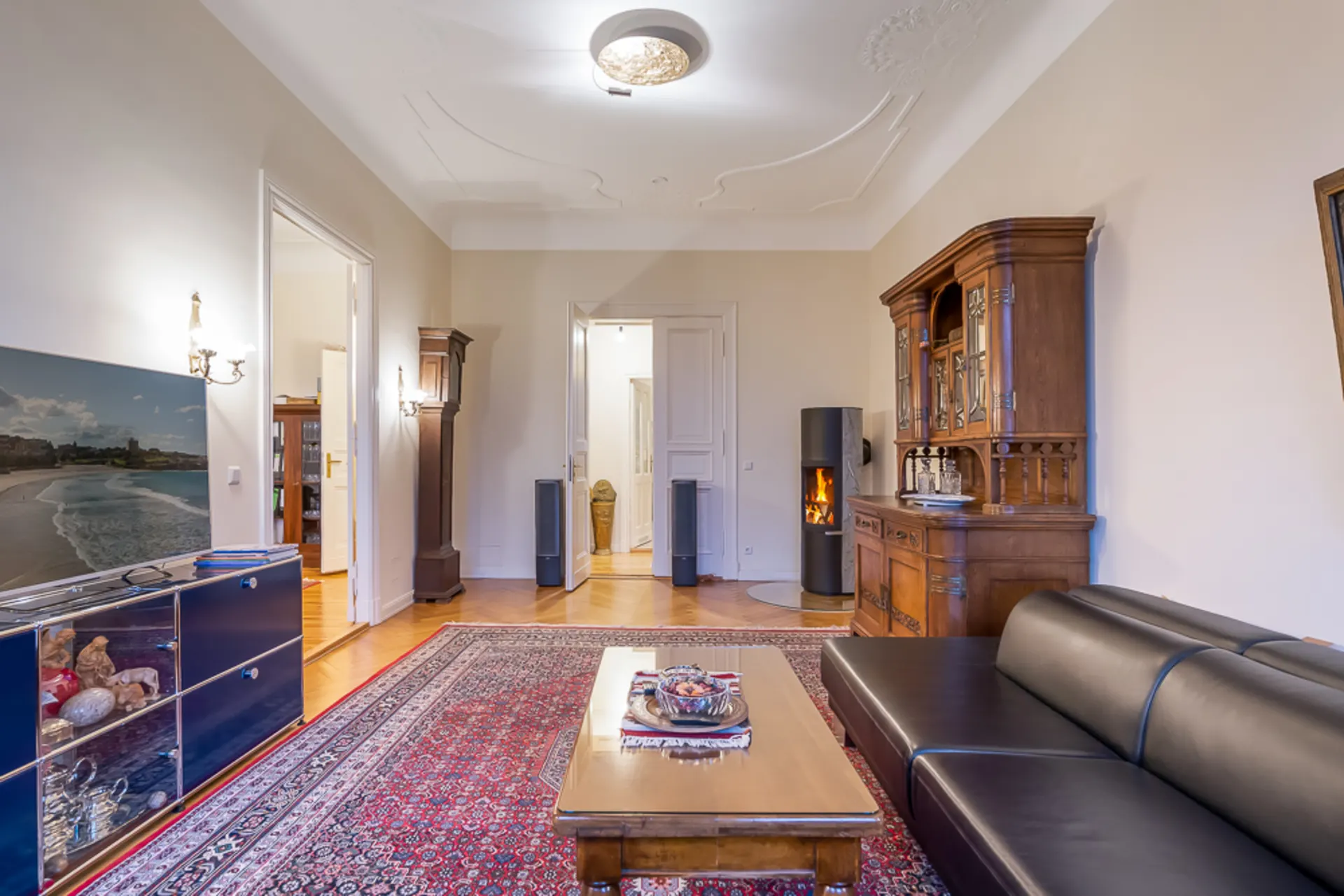 Wohnzimmer mit schwarzem Sofa, Holzschrank, Kamin, Teppich und Couchtisch.