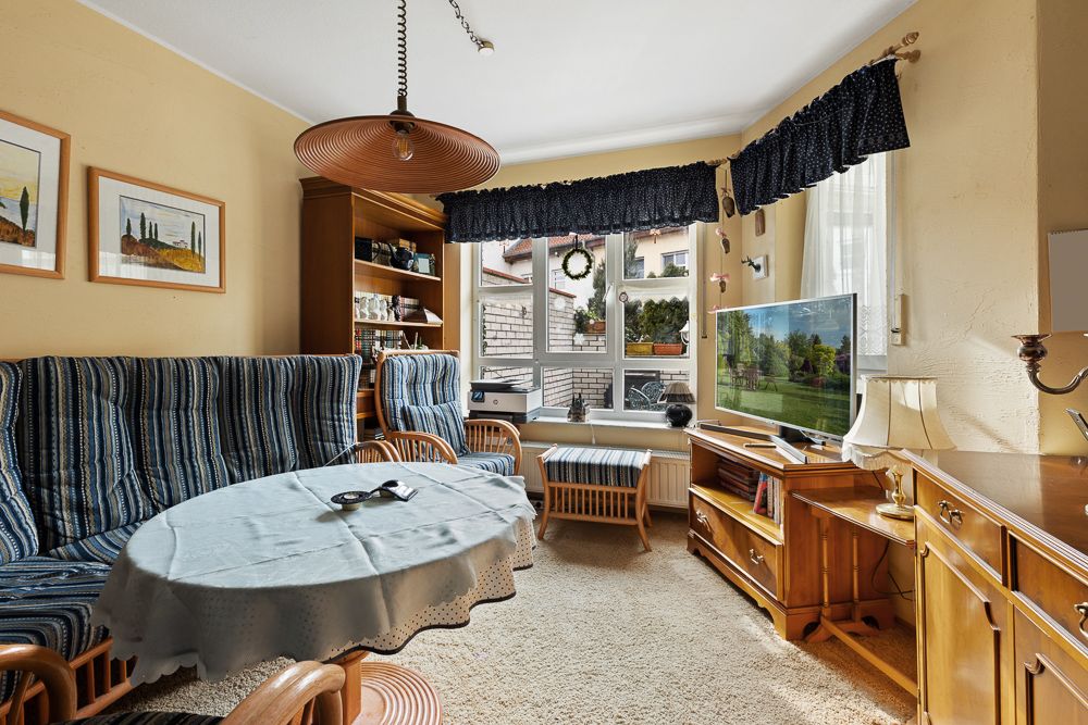 Gemütliches Wohnzimmer mit blauen Polstermöbeln, Holzschrank, TV und großem Fenster.