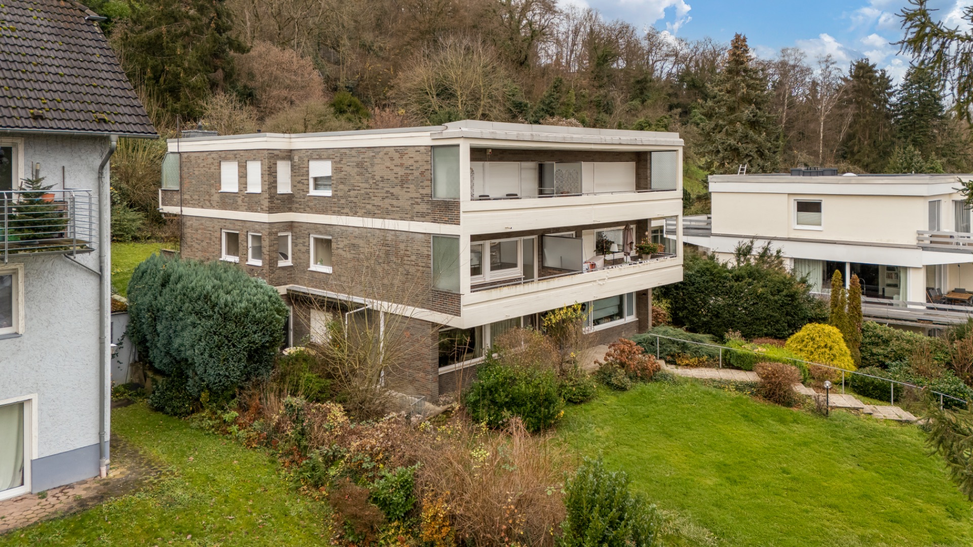 Mehrfamilienhaus mit mehreren Balkonen und großem grünen Garten, umgeben von Bäumen.