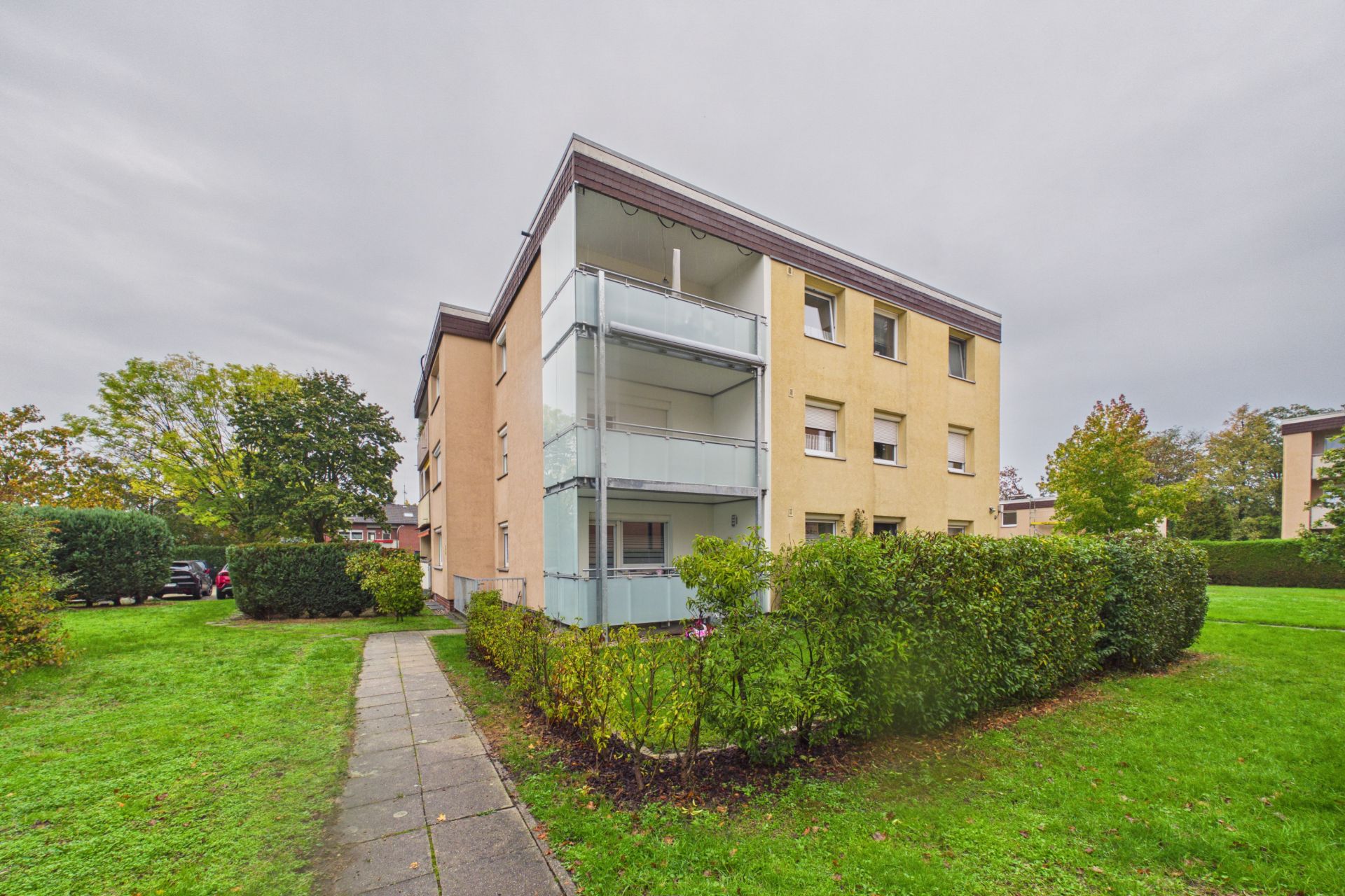 Dreistöckiges Wohnhaus mit Balkonen und umgebendem Grün.