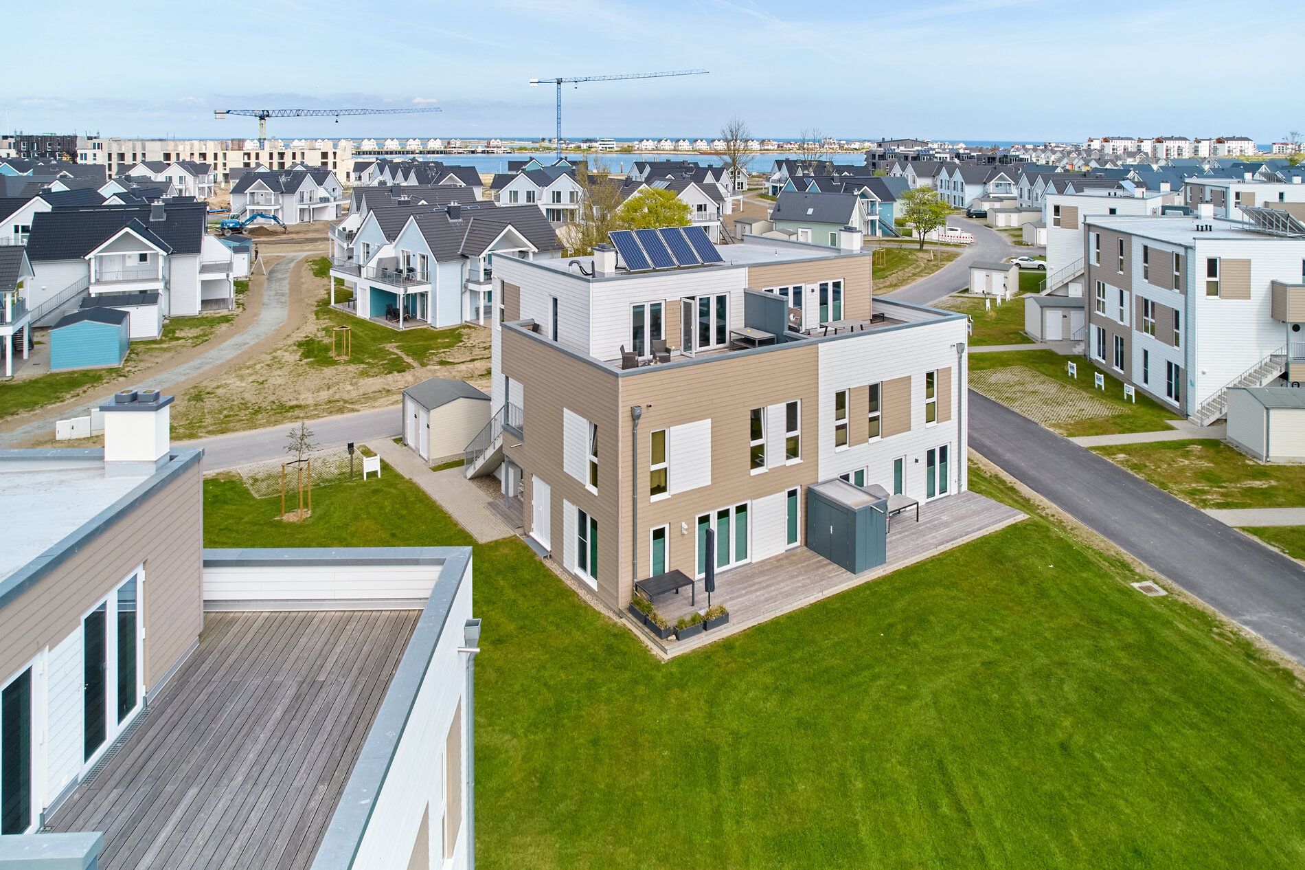 Mehrfamilienhaus mit Terrasse und Solarpanelen, umgeben von weiteren modernen Wohnhäusern.