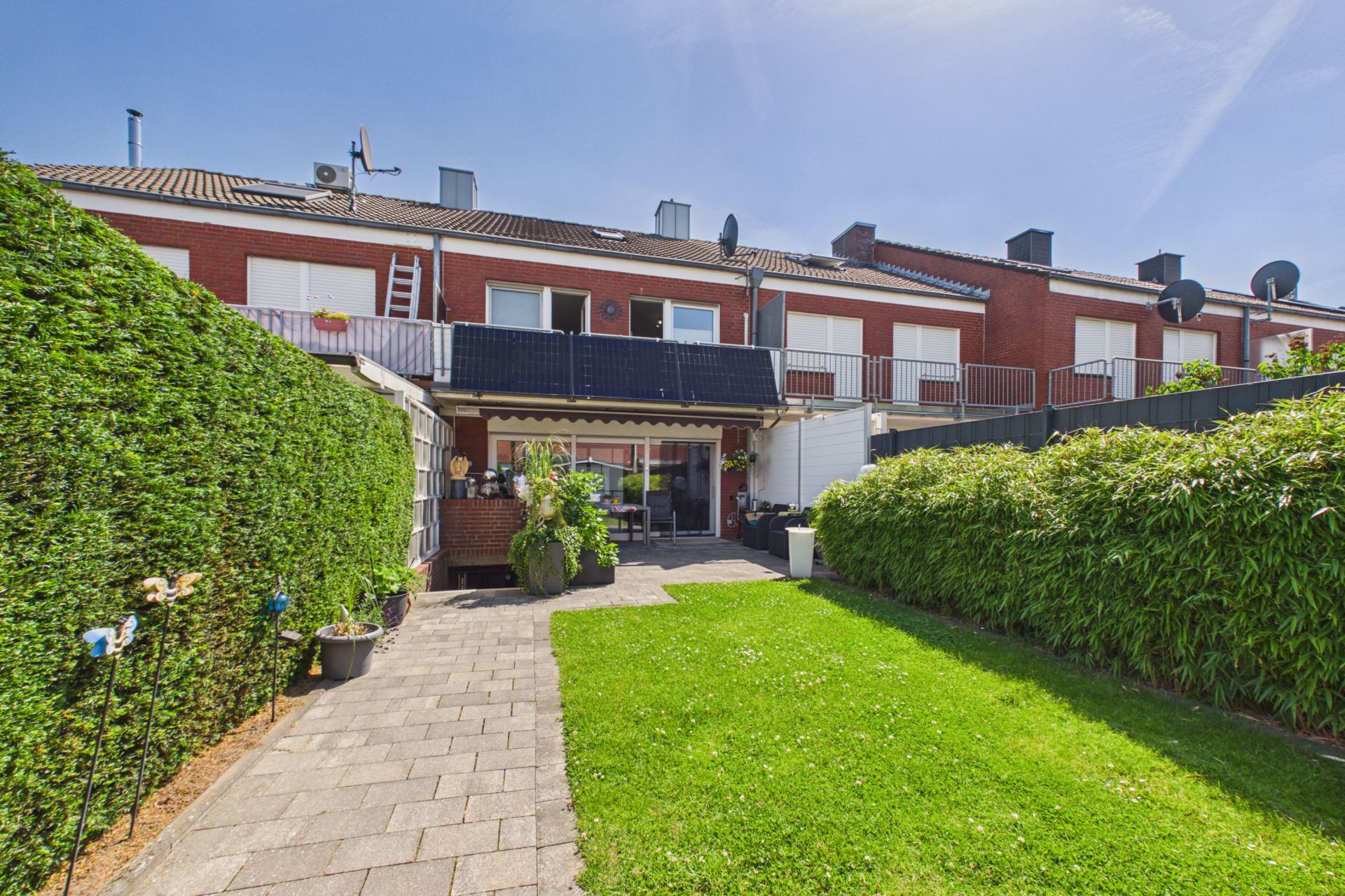 Gepflegter Garten mit Rasen, Terrasse, Hecken und Blick auf ein Reihenhaus.
