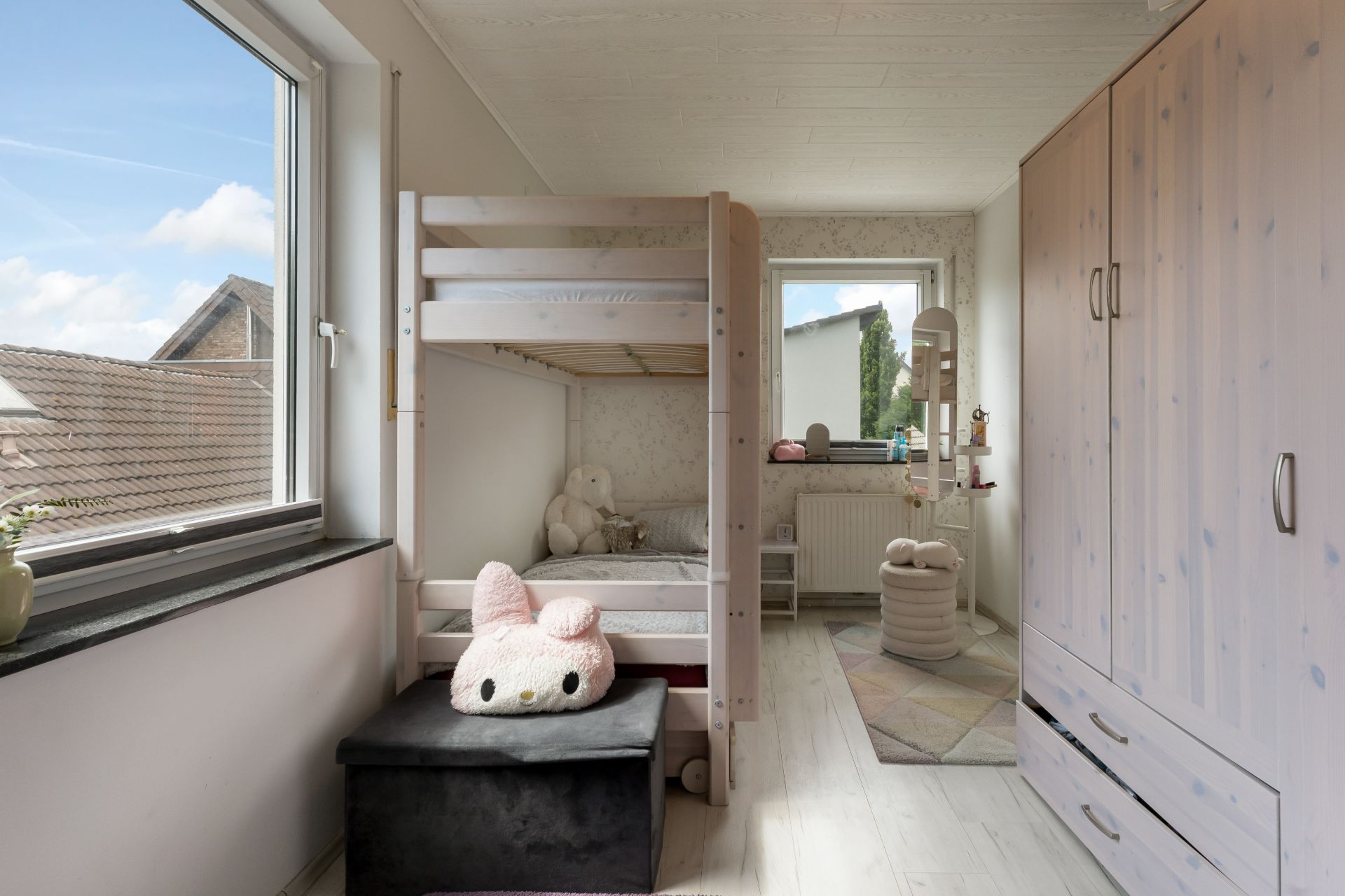 Kinderzimmer mit Etagenbett, großem Schrank, zwei Fenstern und Plüschtieren.