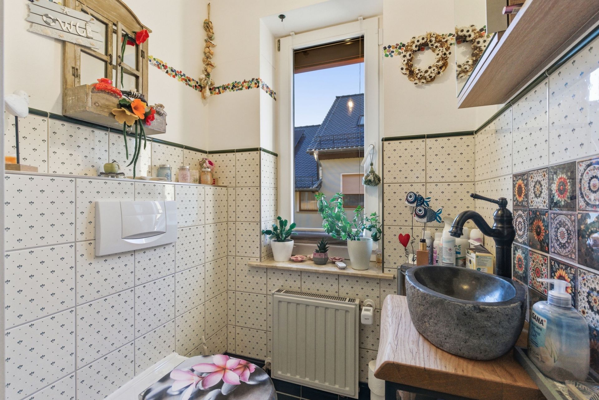 Kleines Badezimmer mit Waschbecken, Fenster, Toilette und dekorativen Fliesen.